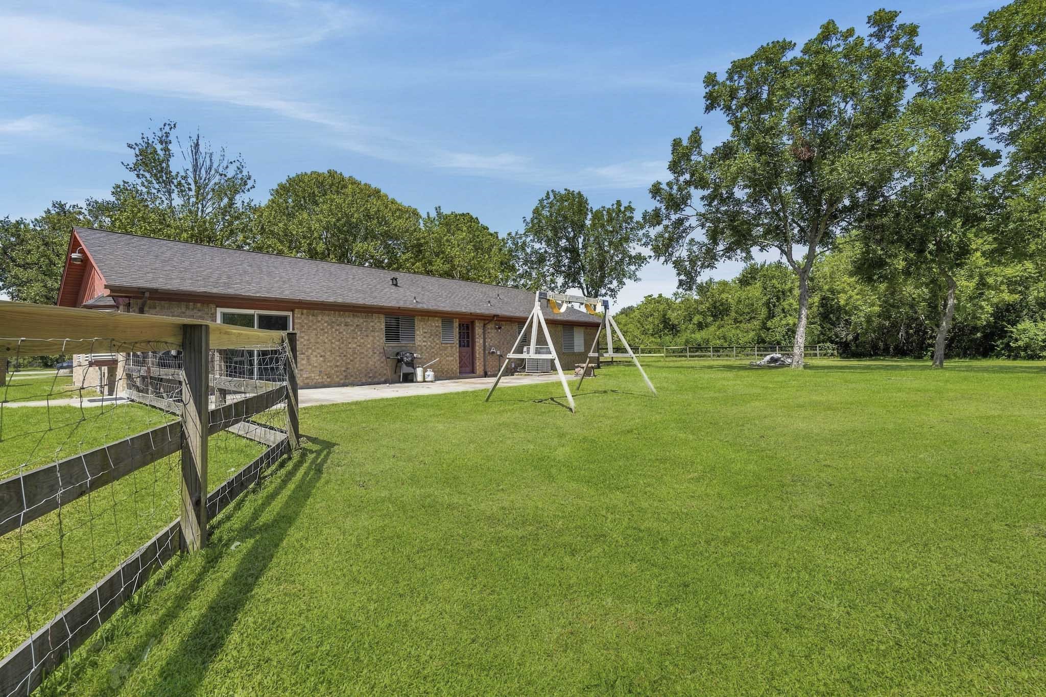 Expansive backyard with lush green lawn, mature trees, and a charming swing set, perfect for outdoor enjoyment and relaxation.