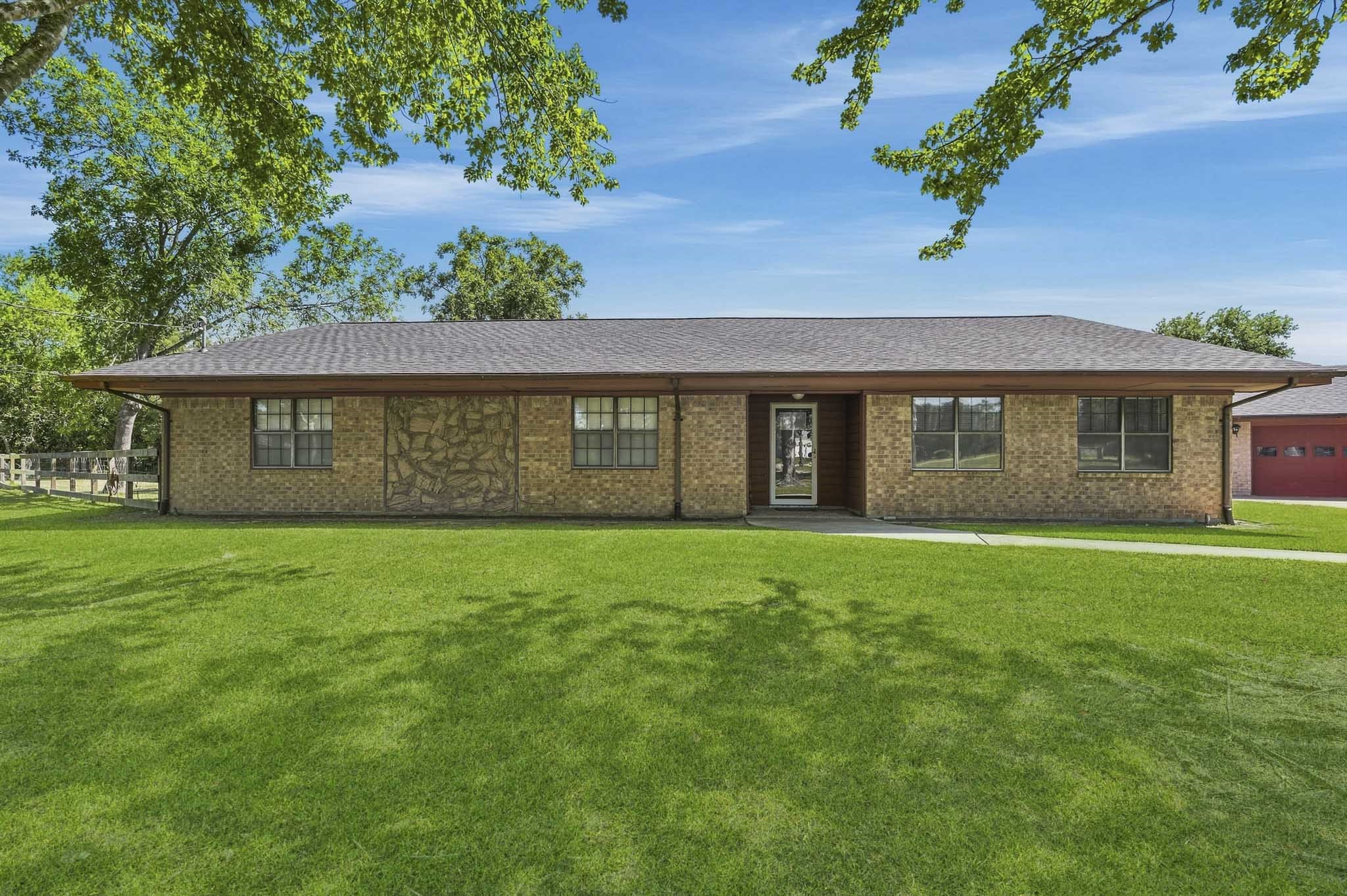 Charming single-story brick home with a spacious front lawn and mature trees, offering a peaceful and inviting atmosphere.