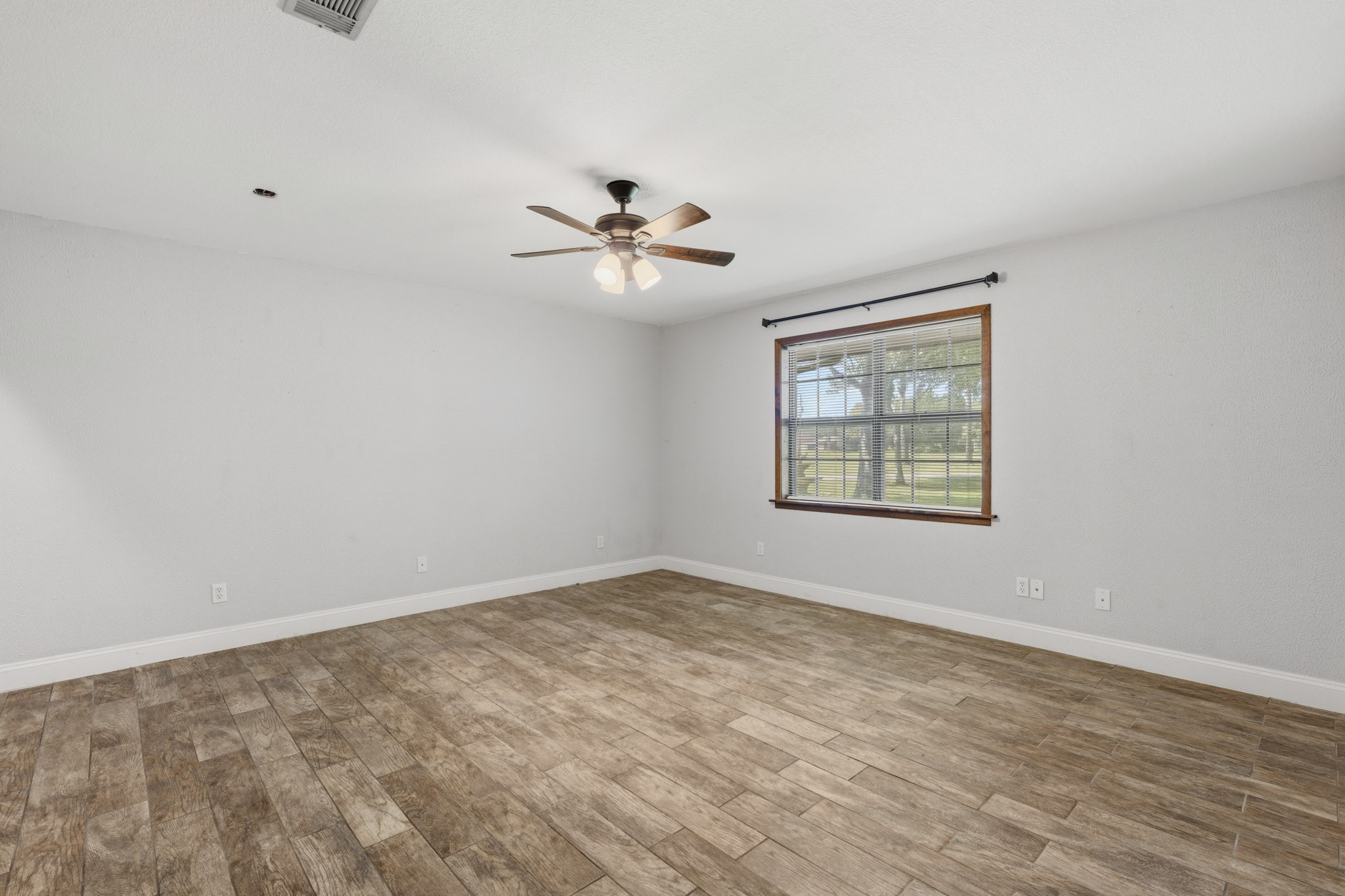 Spacious third bedroom with elegant wood-look flooring, a ceiling fan, and a large window offering serene views.