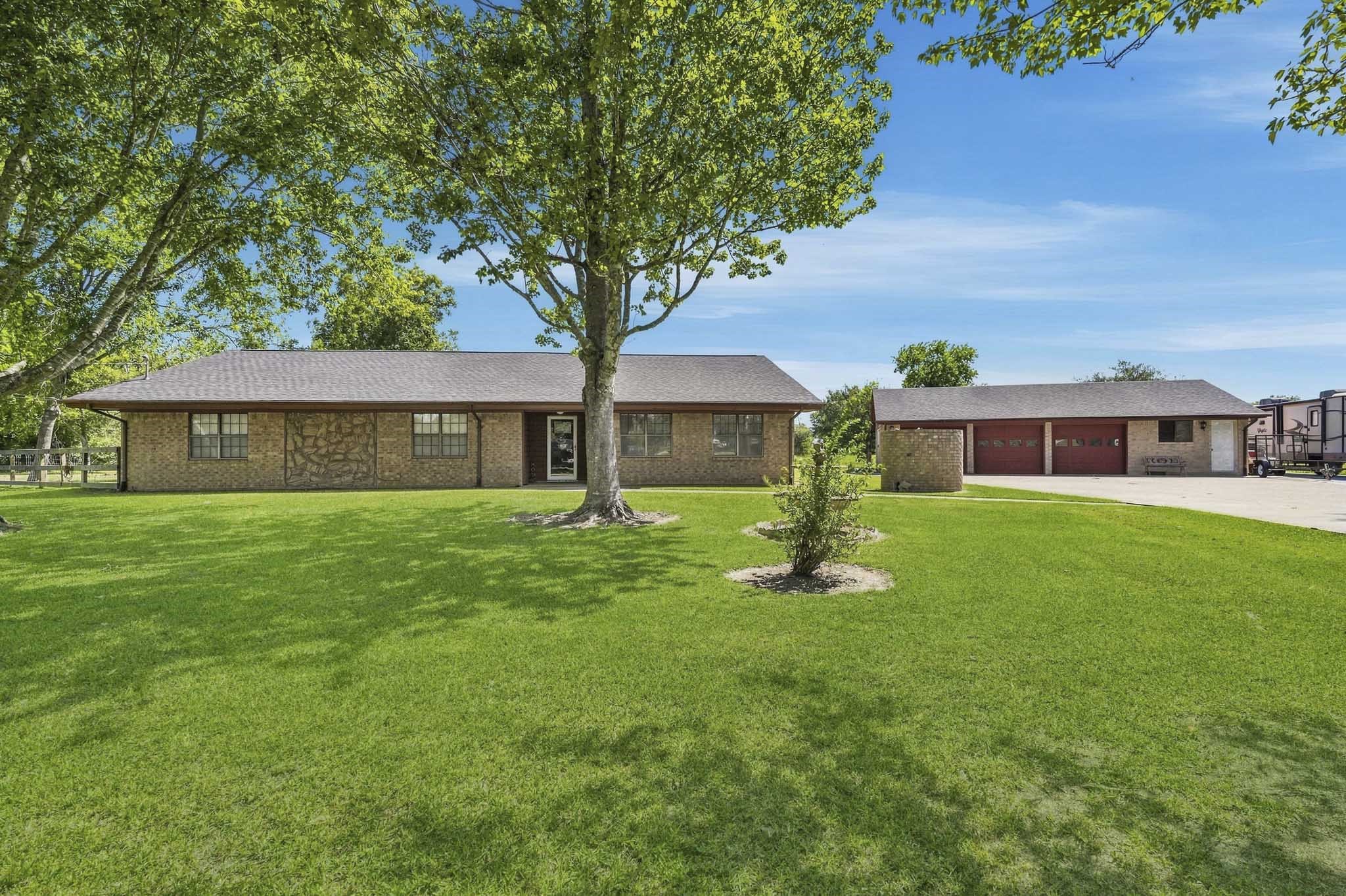 Charming brick ranch-style home with a spacious front lawn and mature trees, featuring a detached garage and ample driveway space.