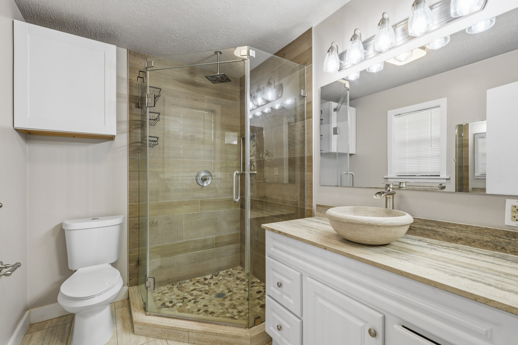 Elegant primary bathroom featuring a modern glass-enclosed shower with stone accents, a stylish vessel sink, and ample lighting.