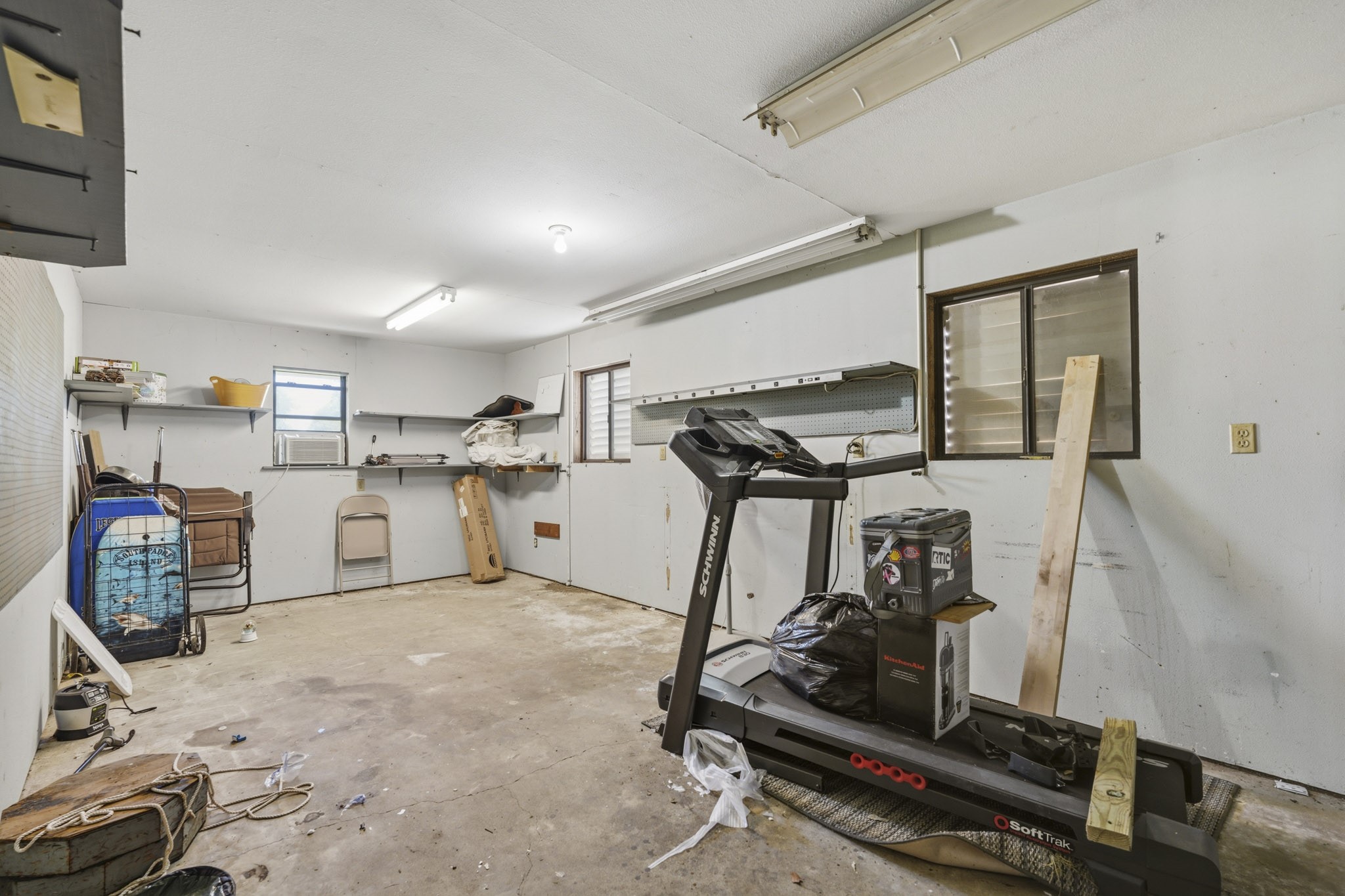 Spacious garage with ample storage options, featuring built-in shelves and windows for natural light. Perfect for a workshop or home gym setup.