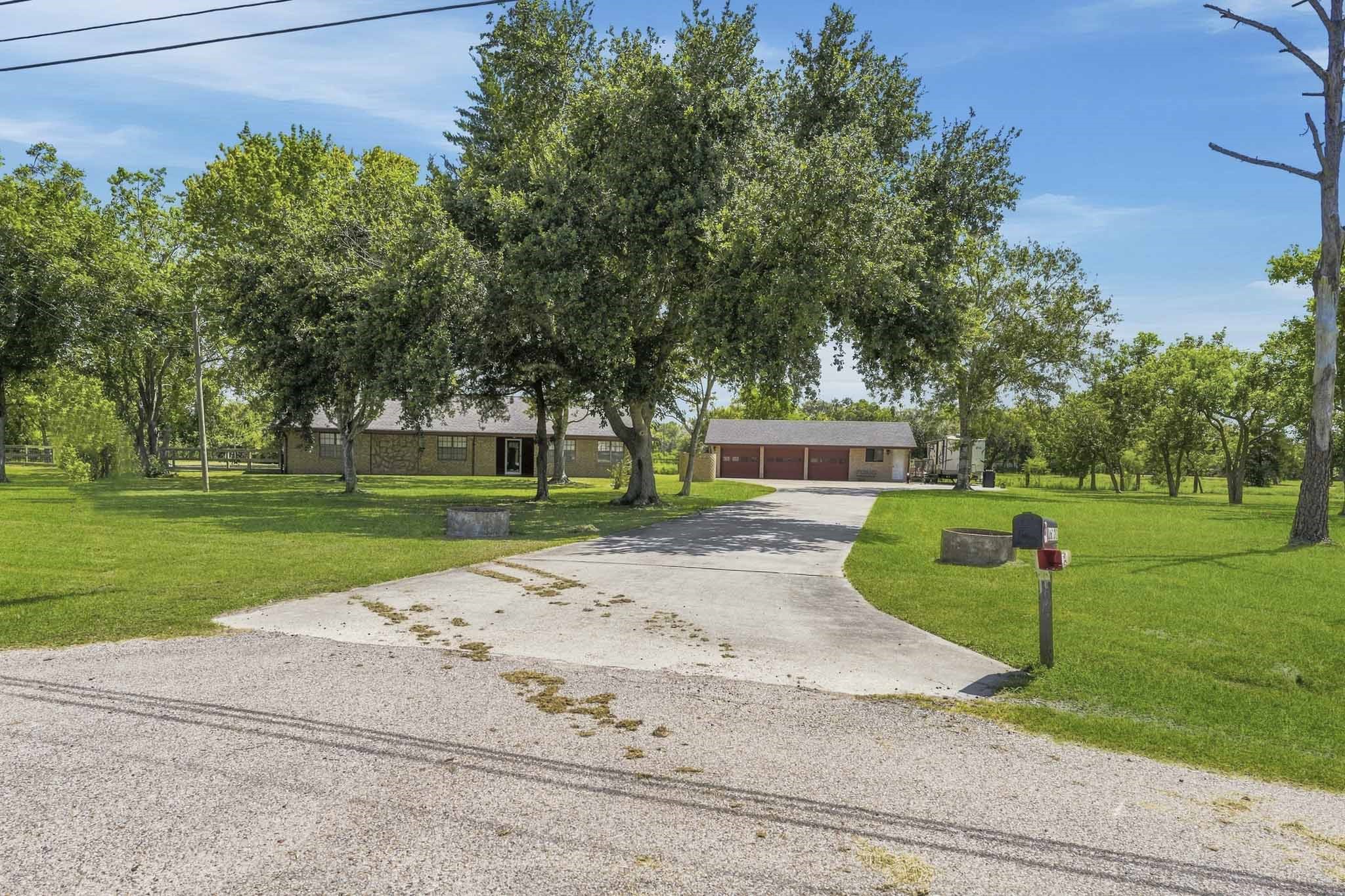Charming countryside home nestled among mature trees, featuring a spacious driveway leading to a detached multi-car garage, all set on expansive, lush green grounds.