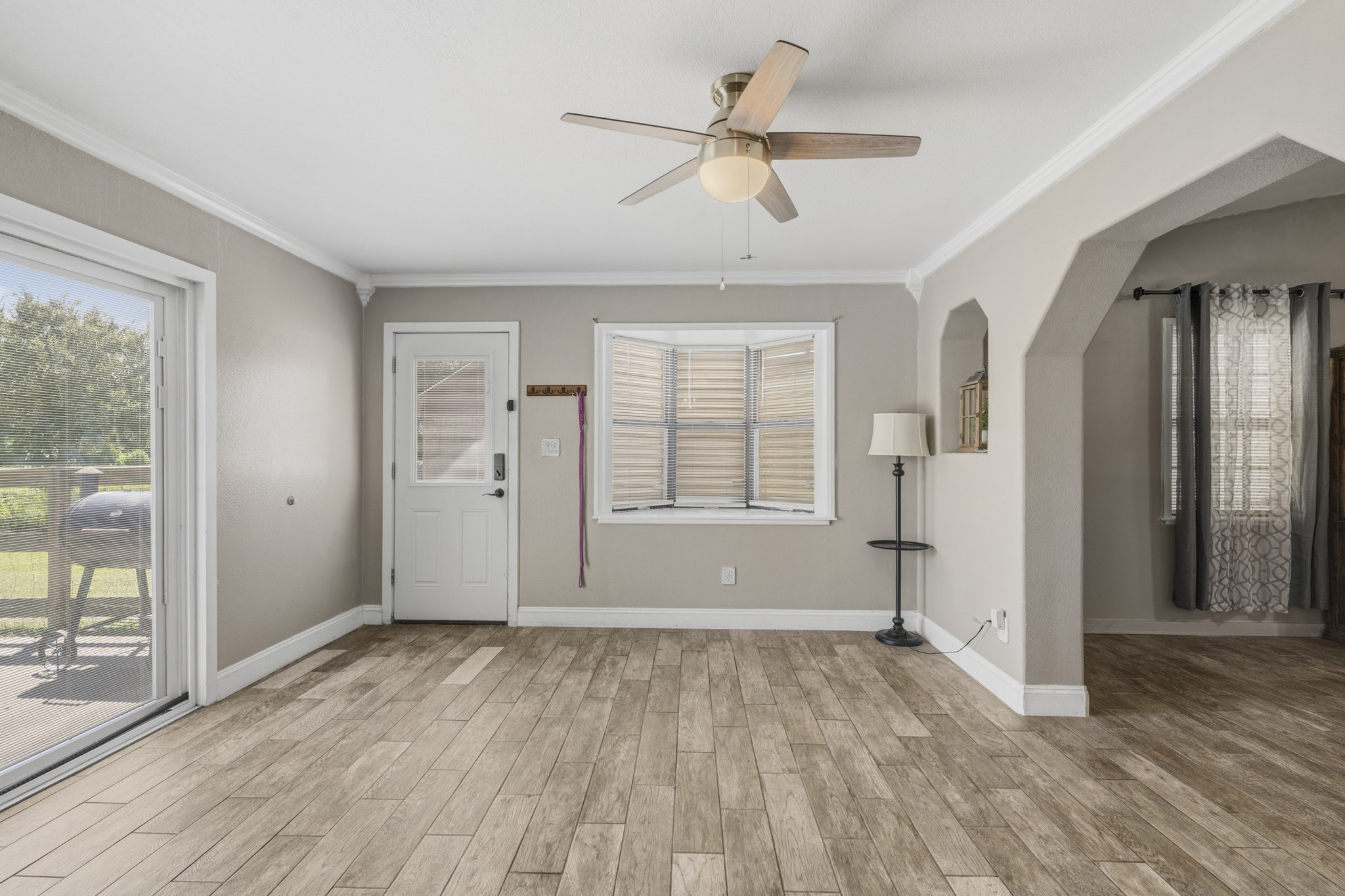 Bright and inviting space with wood-look flooring, a ceiling fan, and ample natural light from large windows and a glass door leading to the outdoor area.