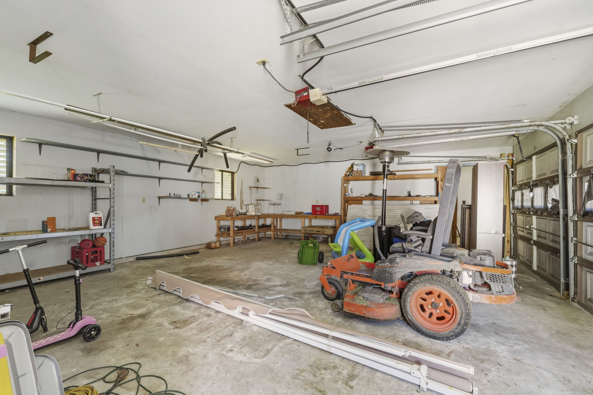 Spacious garage with ample storage shelves, workbench, and room for multiple vehicles. Ideal for hobbyists or extra storage.