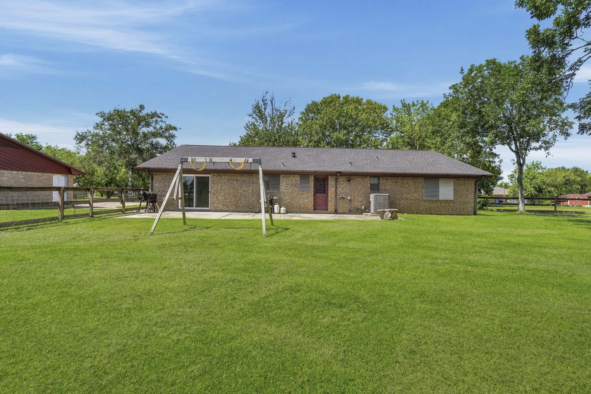 Charming brick home with a spacious backyard, perfect for outdoor activities, featuring a swing set and surrounded by lush greenery. Ideal for living and entertaining.