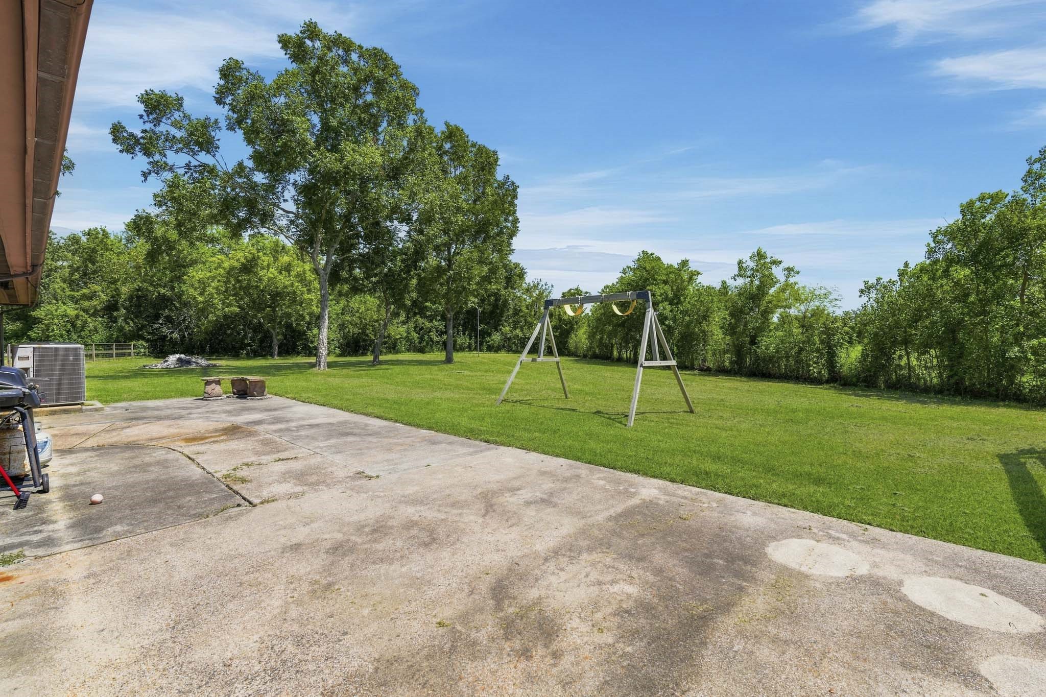 Expansive backyard with a spacious patio, lush greenery, and a swing set, perfect for outdoor activities and relaxation.
