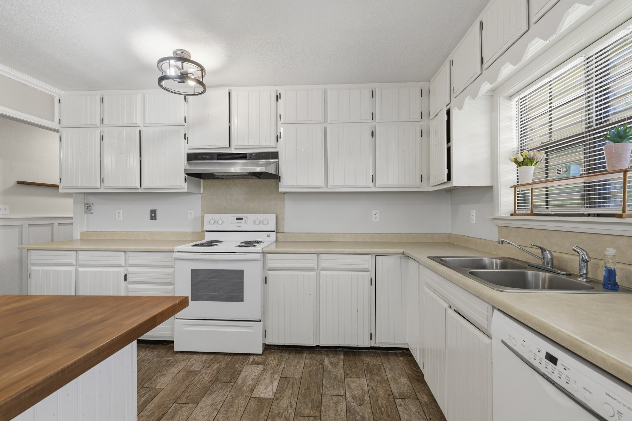Charming kitchen with ample white cabinetry, sleek counter-tops. The large window fills the space with natural light, highlighting the modern appliances and wood-look tile flooring.
