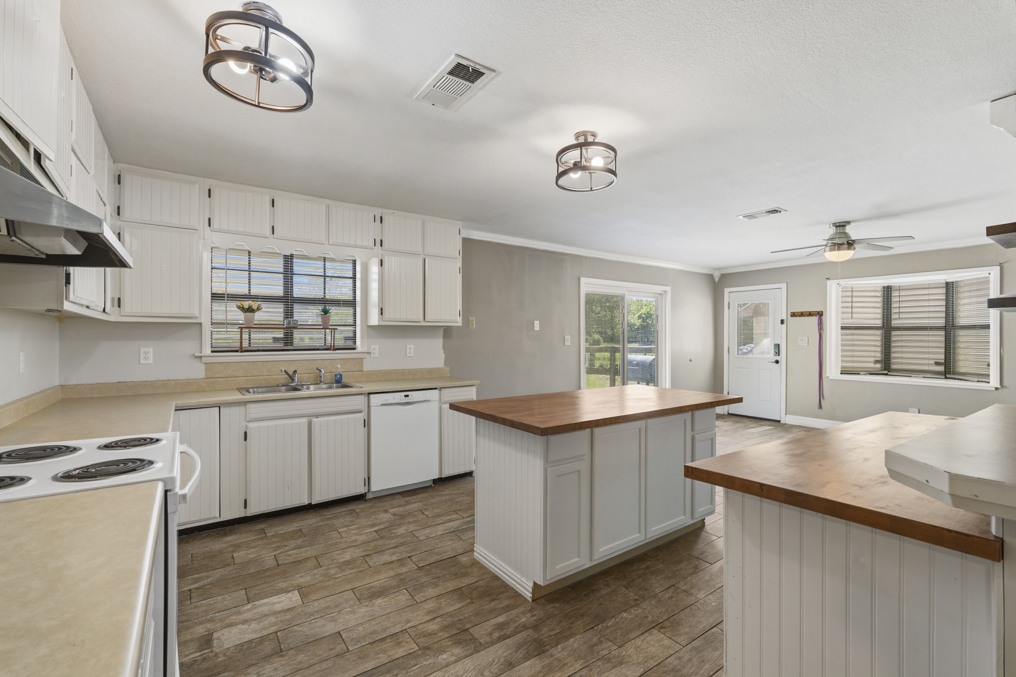 Spacious kitchen with rustic charm features wood-look tile flooring, ample cabinetry, and a central island with wood counter-top complemented by modern lighting and natural light from large windows.