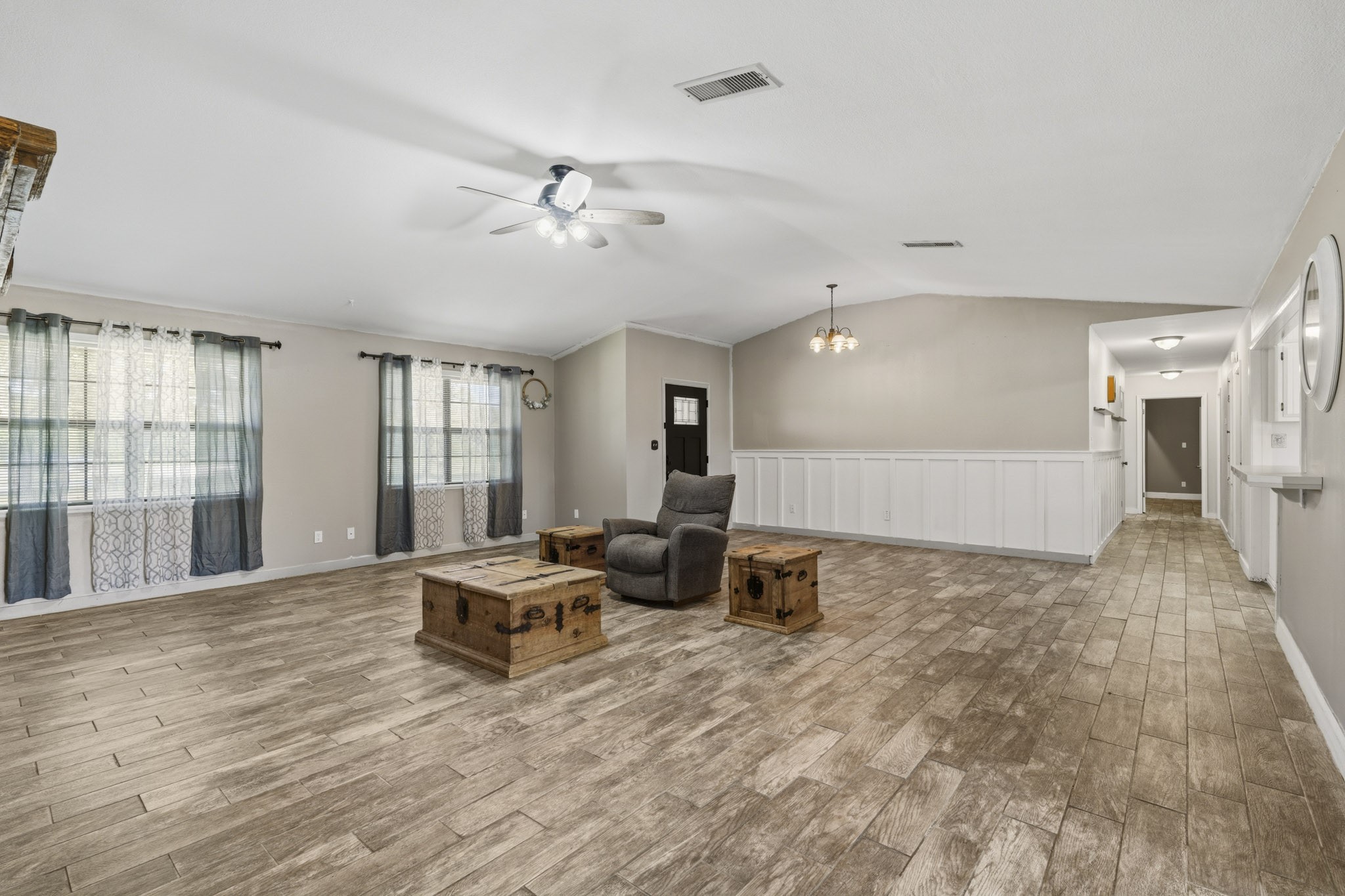 Spacious living area with elegant wood-look flooring, abundant natural light from large windows, and stylish wainscoting, creating an inviting atmosphere perfect for relaxation and entertainment.