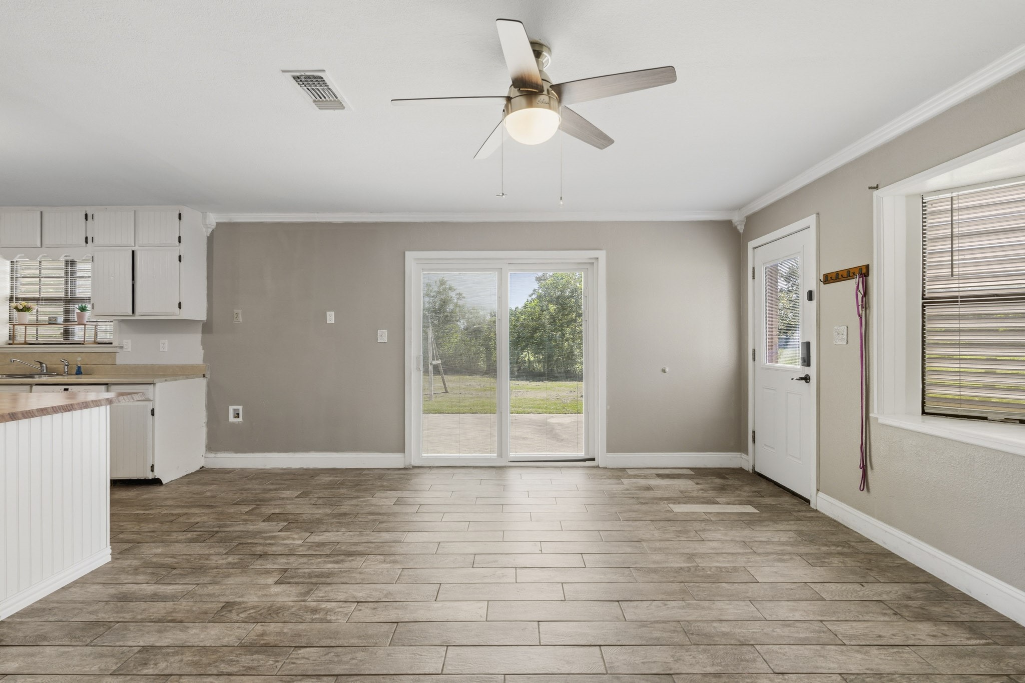 Spacious open-concept dining area featuring wood-look tile flooring, a ceiling fan, and abundant natural light from large sliding doors leading to the backyard.