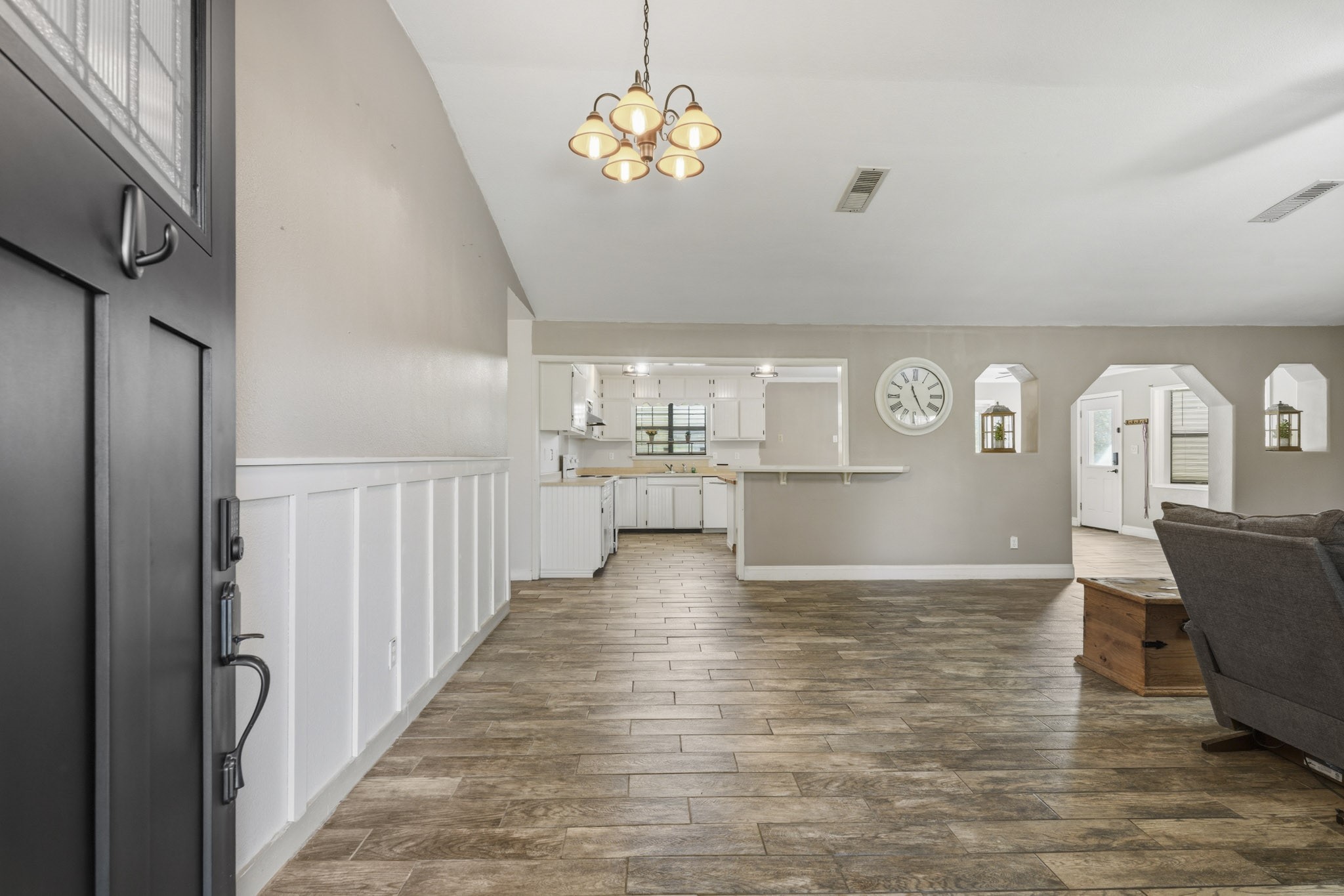 Spacious interior with vaulted ceilings and with elegant wood-look tile flooring, open layout, and a farmhouse style kitchen visible from the entryway. Spacious interior with vaulted ceilings and with elegant wood-look tile flooring, open layout, and a farmhouse style kitchen visible from the entryway.