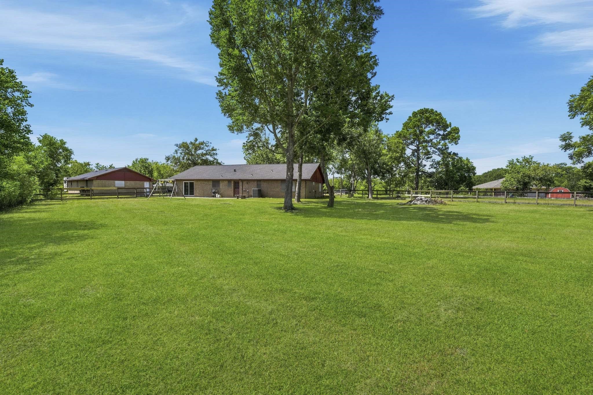Expansive backyard with lush green lawn, mature trees, and a charming brick house offering serene country living.