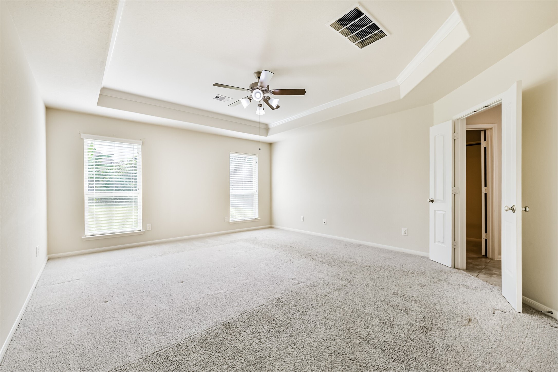Spacious primary bedroom featuring abundant natural light, elegant tray ceiling, and plush carpeting for ultimate comfort.