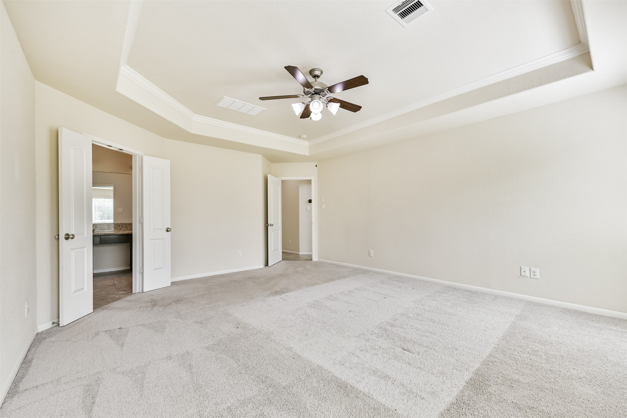 Spacious primary bedroom with elegant tray ceiling, plush carpeting, and an en-suite bathroom for ultimate comfort and convenience.