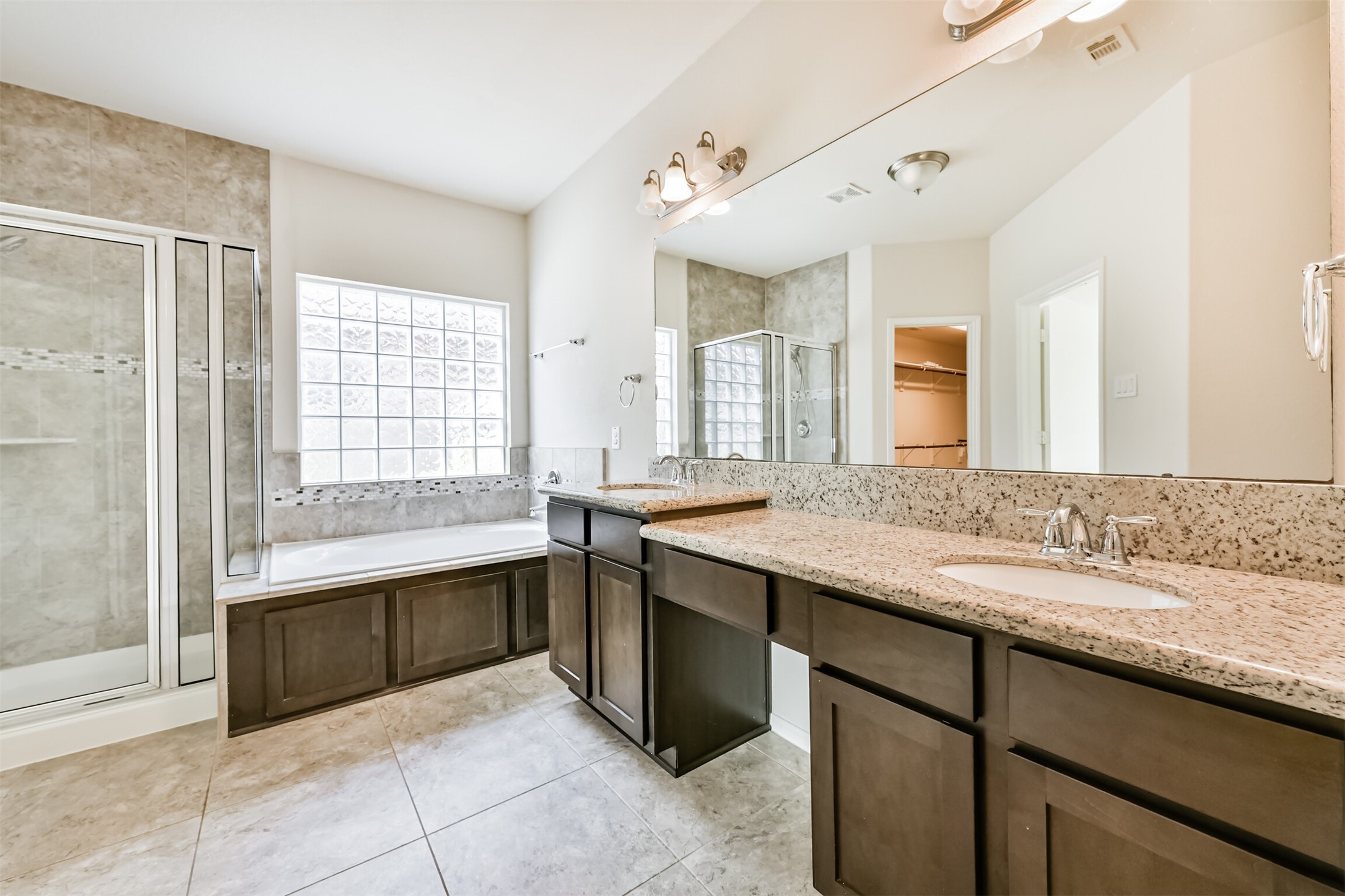 Luxurious primary bath featuring a spacious double vanity, elegant granite countertops, a relaxing soaking tub, and a modern glass-enclosed shower. Perfect for unwinding and rejuvenation.