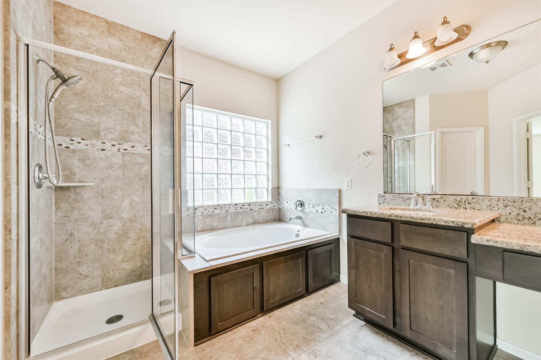 Luxurious primary bathroom featuring a spacious glass-enclosed shower, a relaxing soaking tub, and elegant dual vanities with granite countertops. Perfect for unwinding in style.
