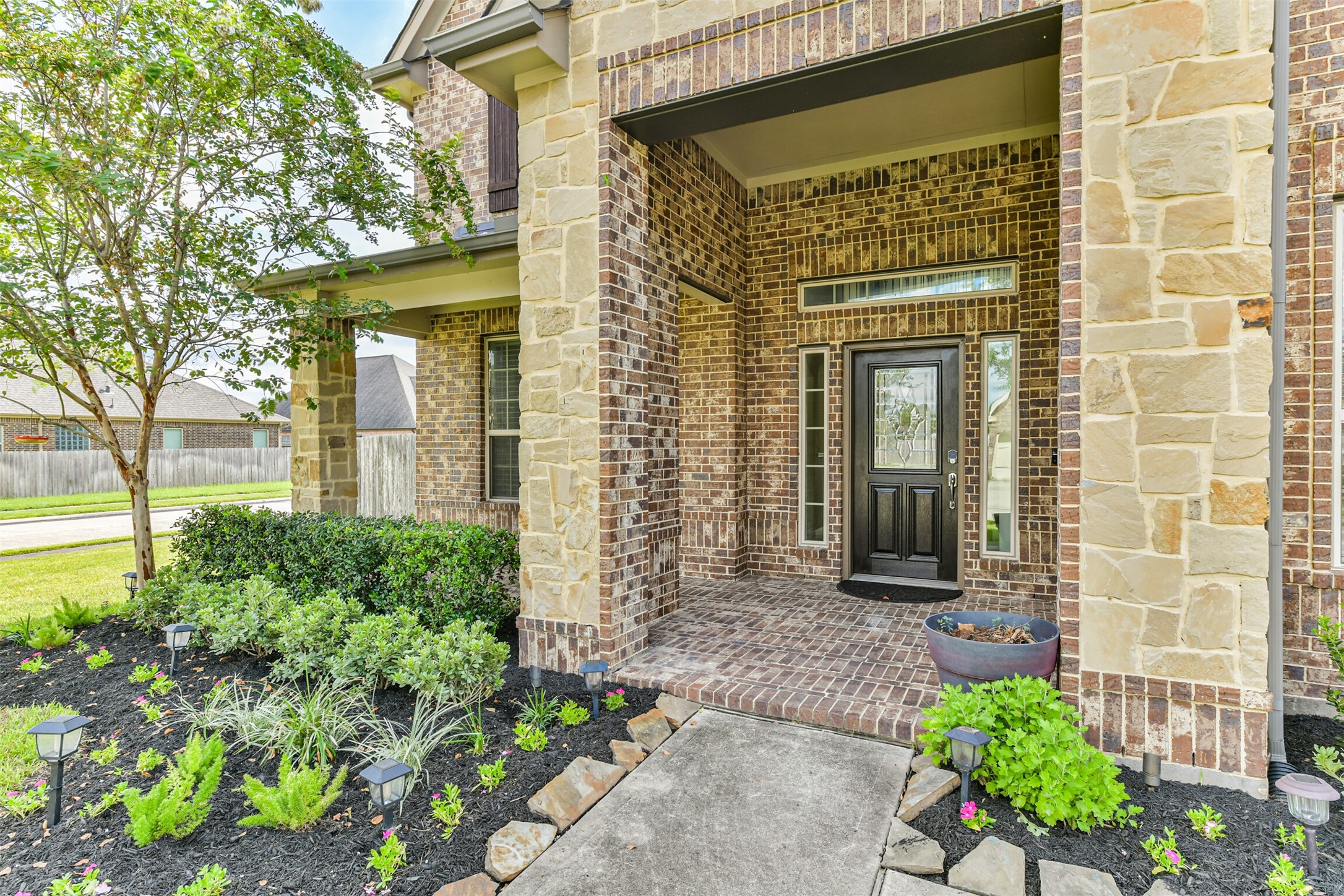 Welcome to your new home! This inviting entry features elegant stonework and lush landscaping, setting the stage for a warm welcome.
