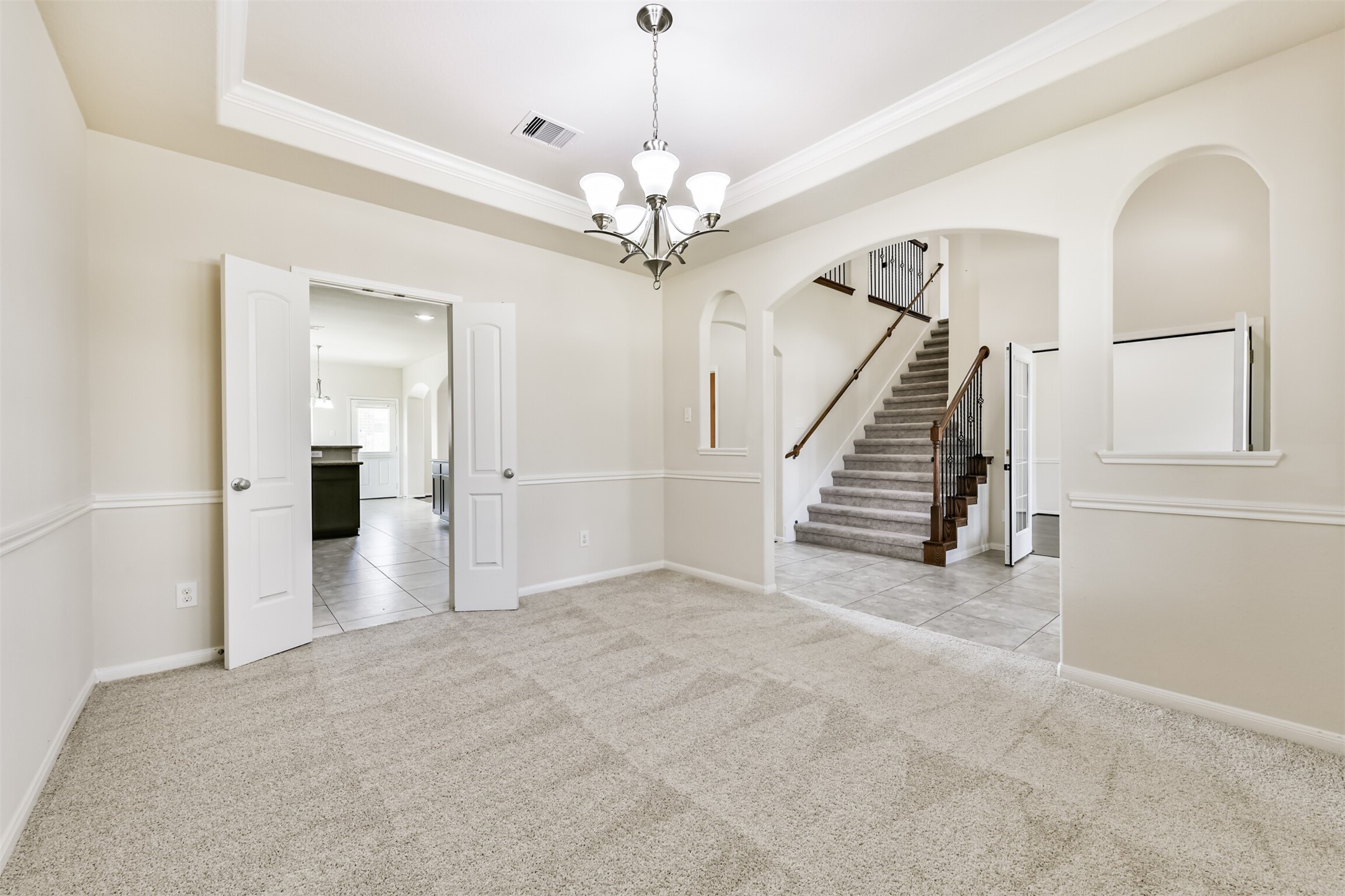 Elegant formal dining room featuring soft carpeting, a stylish tray ceiling, and a chic chandelier, seamlessly connected to the kitchen for effortless entertaining.