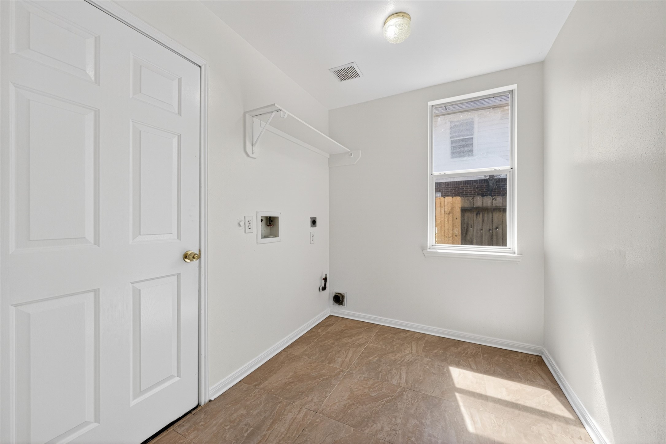 The laundry room provides a bright and practical space for chores, featuring durable tile flooring and a large window that keeps the area feeling fresh and airy.