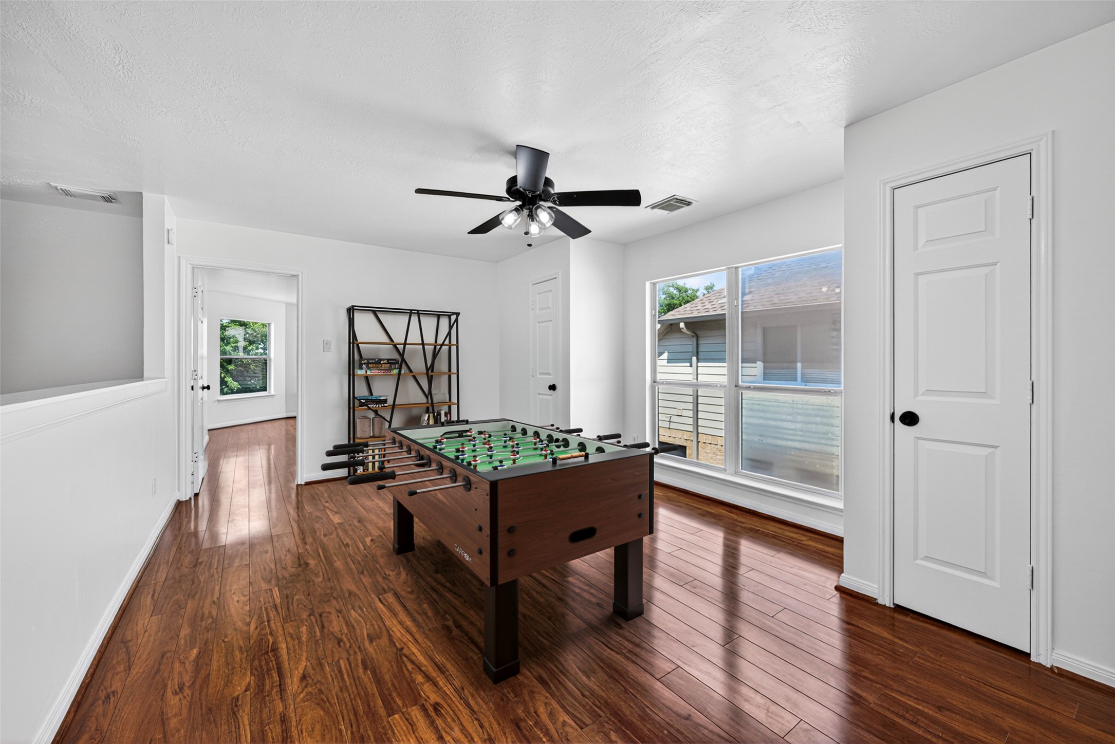 The versatile upstairs game room is a sprawling space anchored by rich wood flooring and bathed in natural light from large windows.