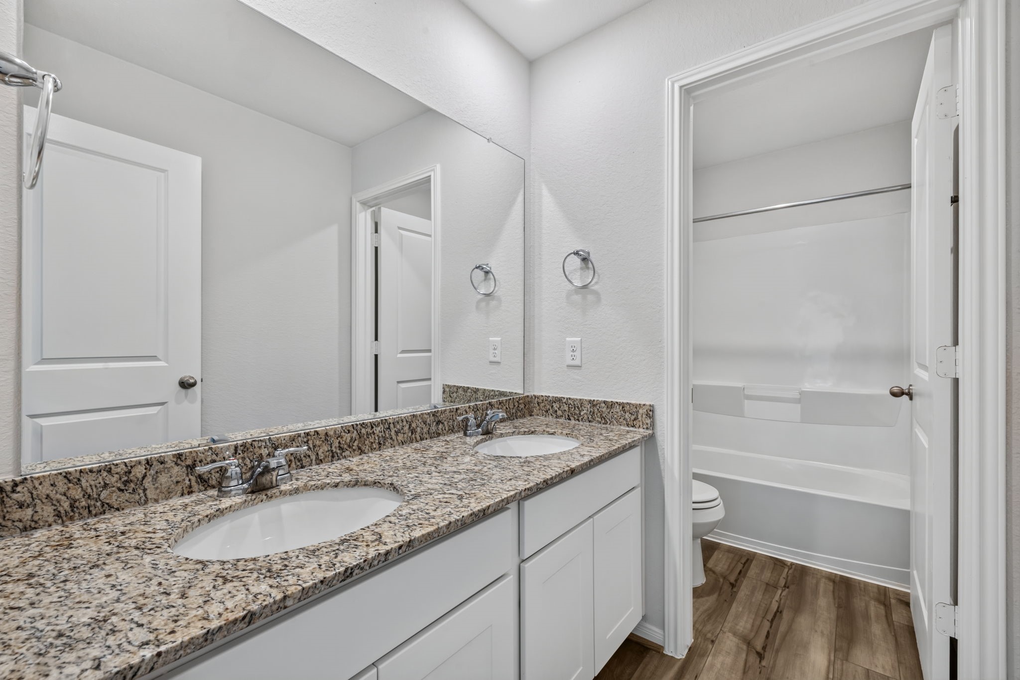 SECONDARY BATHROOM II - The secondary bath has a granite double vanity with white shaker cabinets, plus a separate tub/shower and toilet area behind a door.