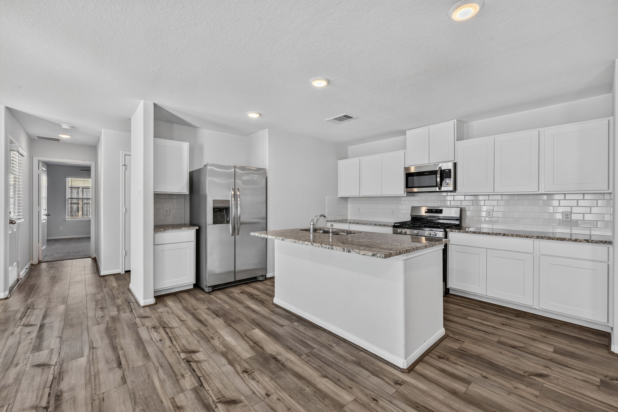 KITCHEN - The kitchen has white shaker cabinets, granite countertops, subway tile backsplash, and a stainless steel appliance package with a side-by-side refrigerator.