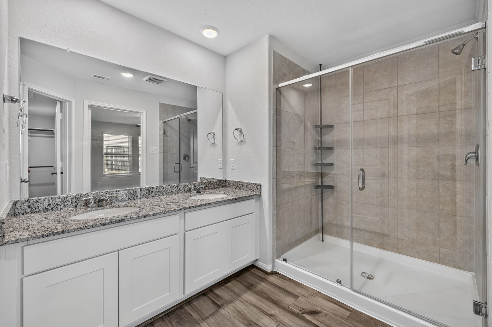 PRIMARY BATHROOM - The primary bath has a granite double vanity, a large walk-in shower with tile surround and glass enclosure, and a view into the walk-in closet.