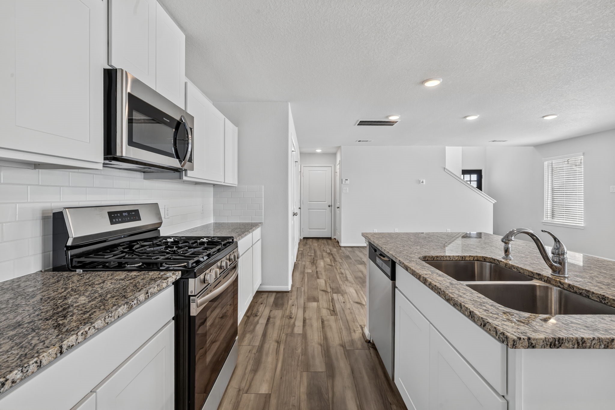 KITCHEN III - The gas range sits beneath a built-in microwave, with plenty of granite counter space and a view through the home toward the stairs, front entry and garage entry.