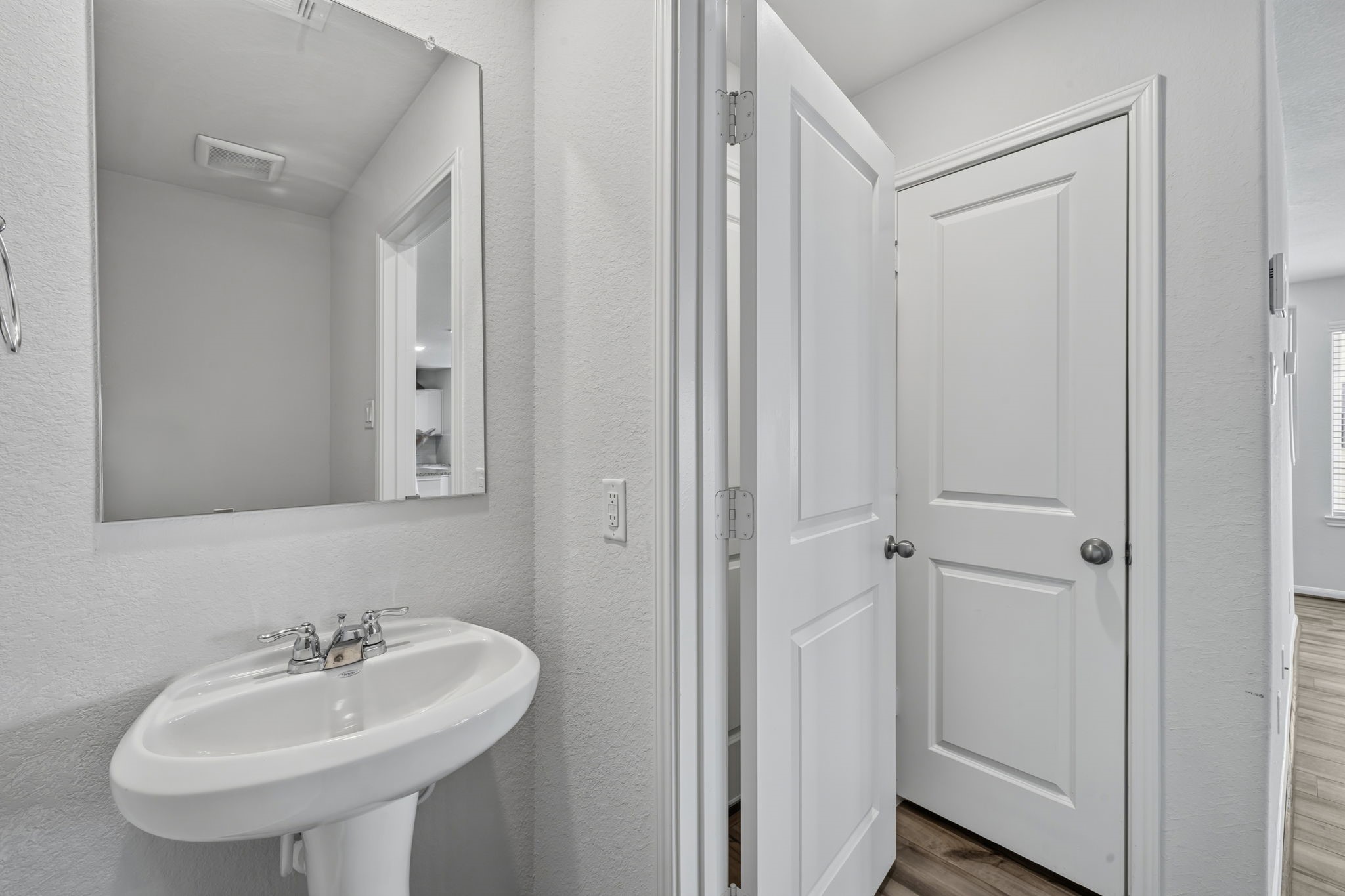 HALF BATH - A convenient first-floor half bath with a pedestal sink and a decorative mirror, just off the main living area.