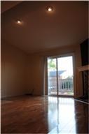 This photo shows a room with high ceilings and recessed lighting, featuring hardwood floors and a sliding glass door leading to an outdoor space. There's also a fireplace, adding a cozy touch.