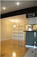 This photo showcases a bright, open living area with polished wood flooring, built-in shelving, and recessed lighting. There's a partial view of a kitchen bar area, adding a modern touch.
