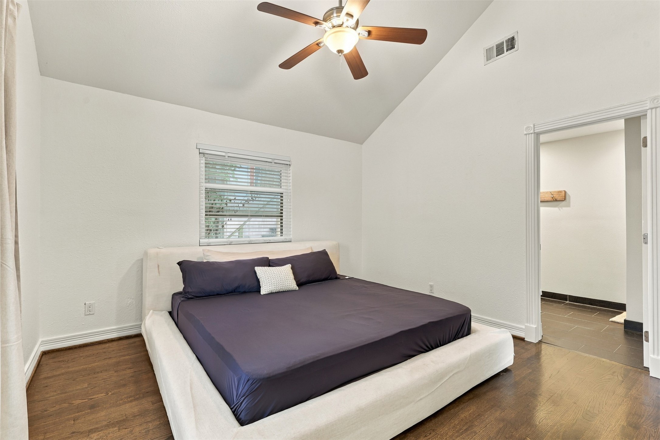Spacious bedroom with vaulted ceiling, elegant ceiling fan, and rich hardwood floors, offering a serene retreat.