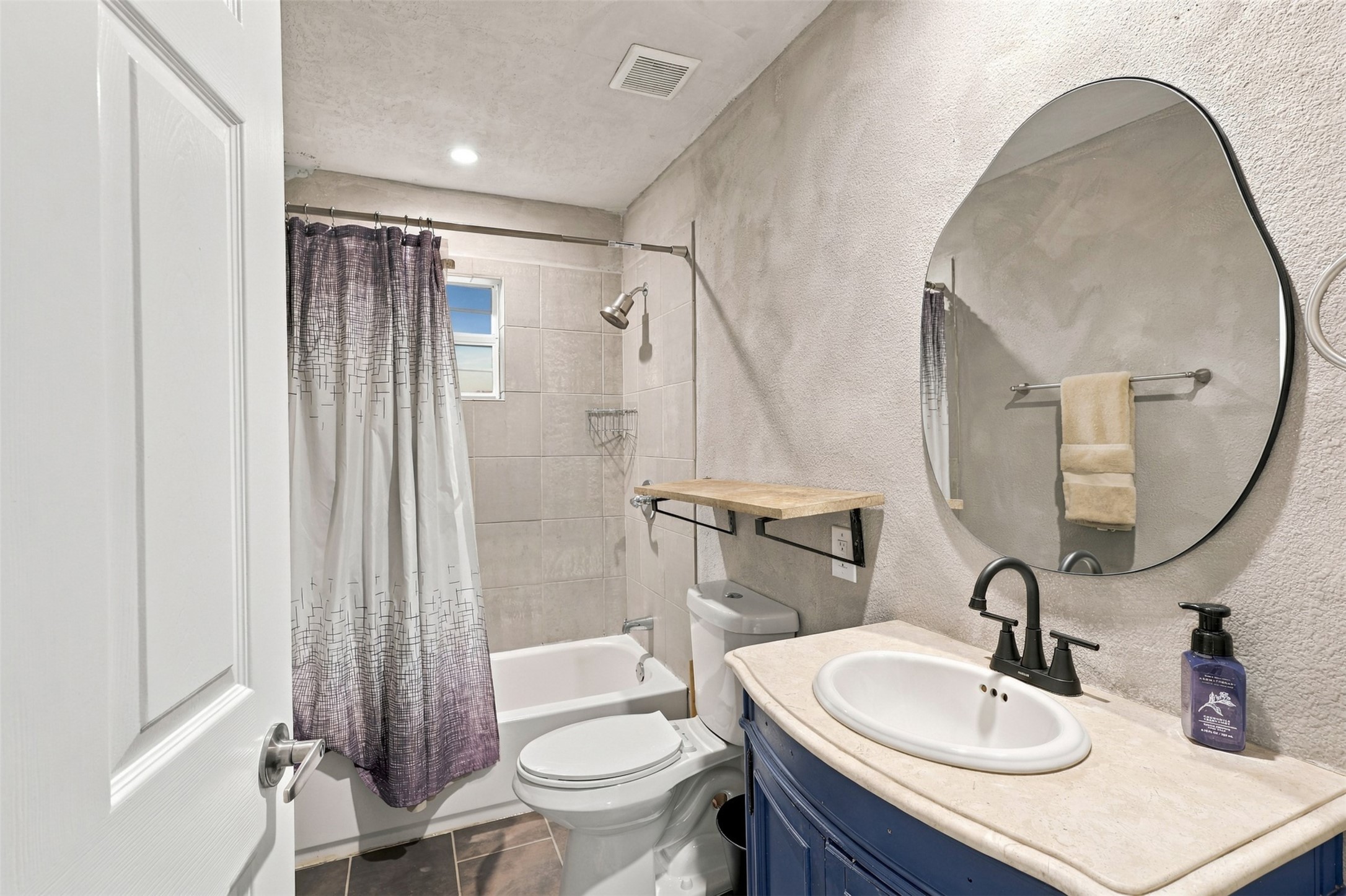 Charming bathroom featuring a sleek oval mirror, modern fixtures, and a cozy tub with shower.