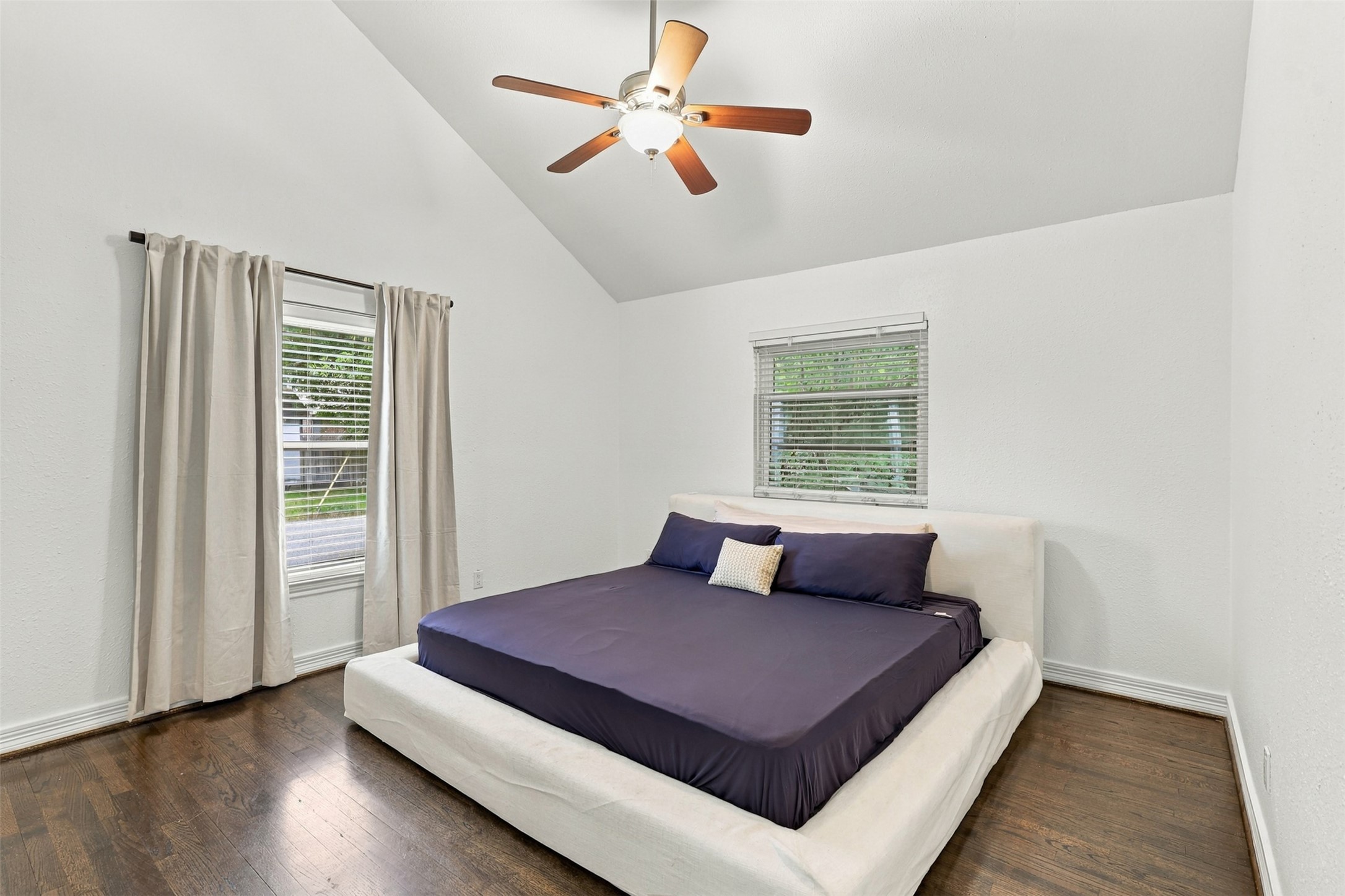 Spacious bedroom with vaulted ceilings, featuring a modern ceiling fan and large windows for ample natural light.