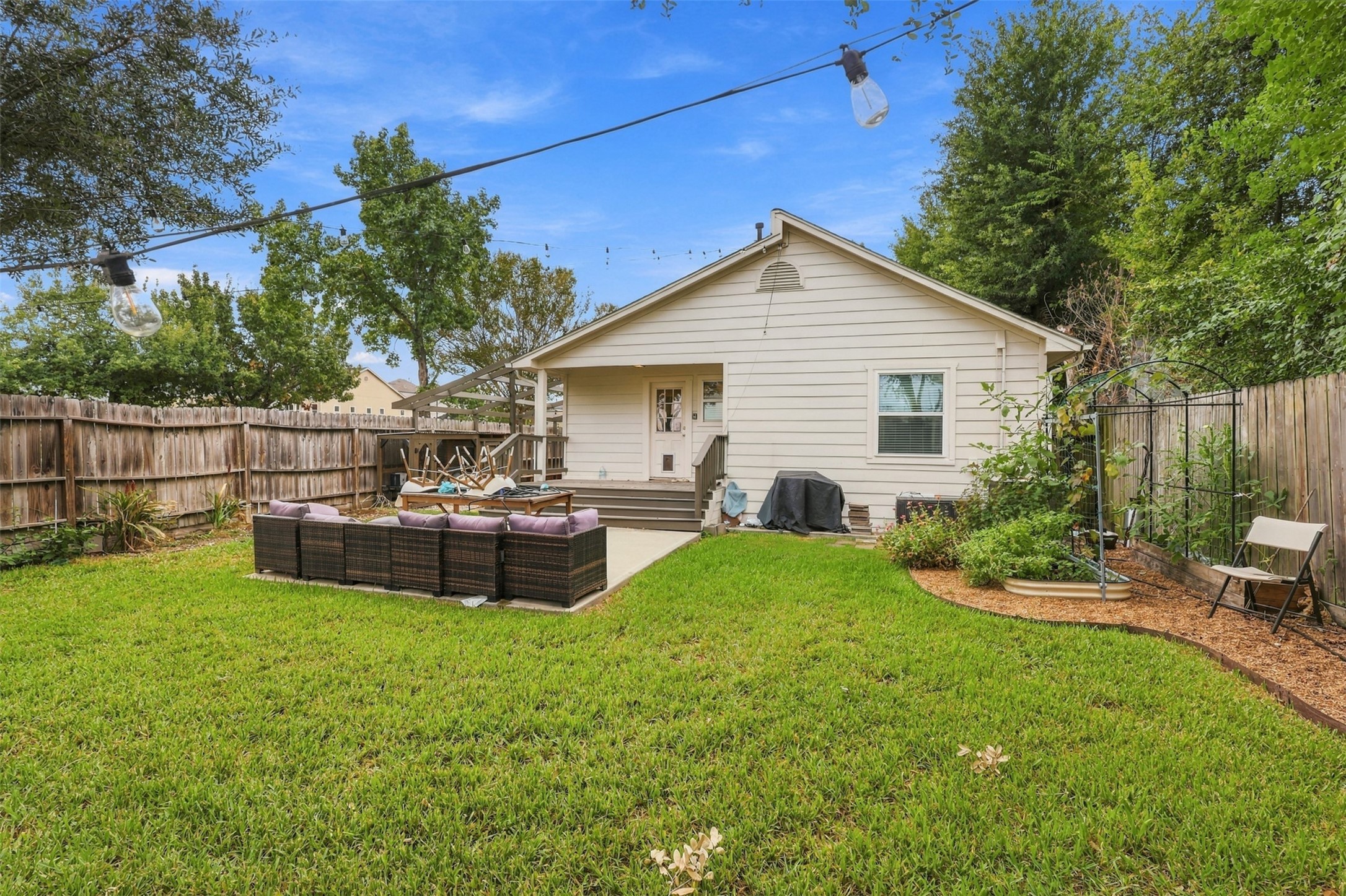 Charming backyard oasis featuring a cozy patio area with comfortable seating, surrounded by lush greenery and a privacy fence, perfect for relaxation and outdoor gatherings.