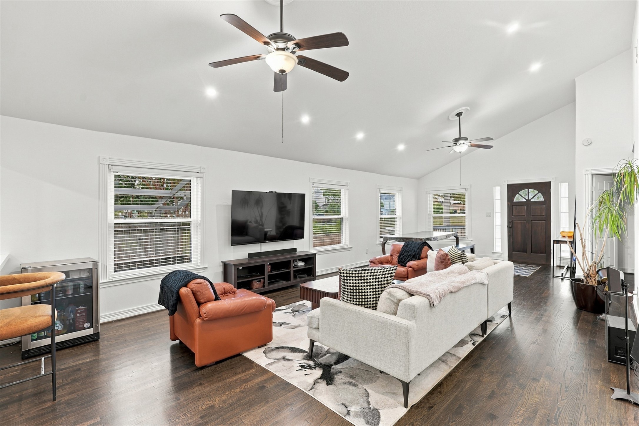 Spacious and inviting living area features high ceilings, hardwood floors, and abundant natural light from multiple windows, complemented by modern ceiling fans and a cozy seating arrangement.