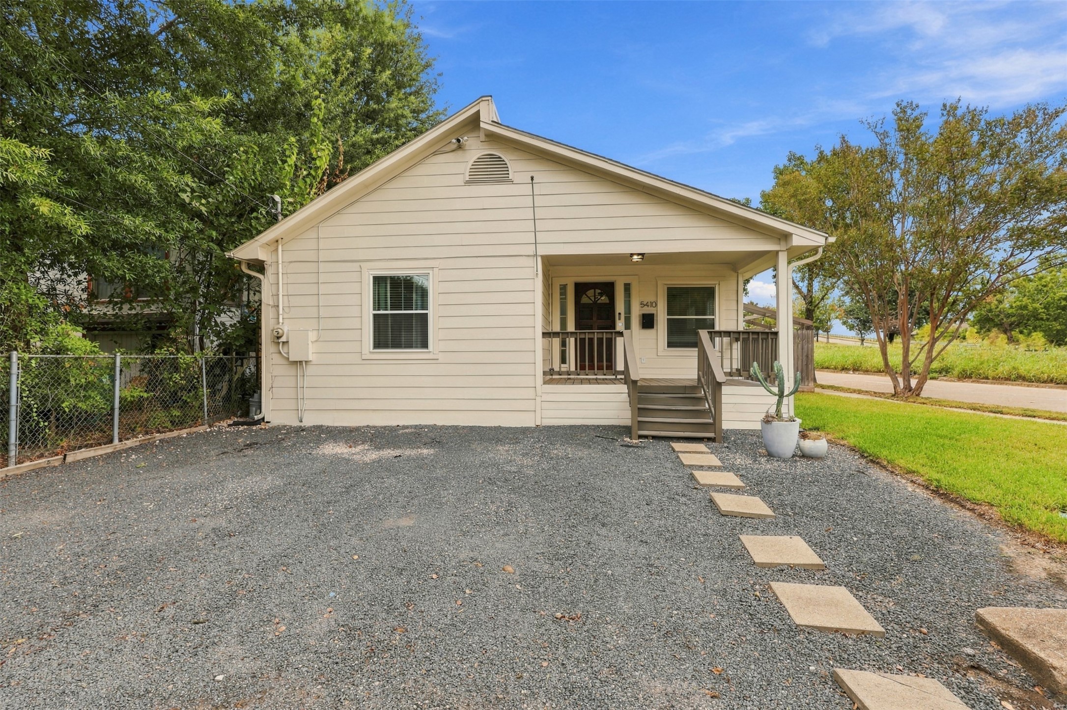 Charming single-story home with a welcoming front porch, framed by lush greenery and a spacious driveway, perfect for easy access and outdoor relaxation.