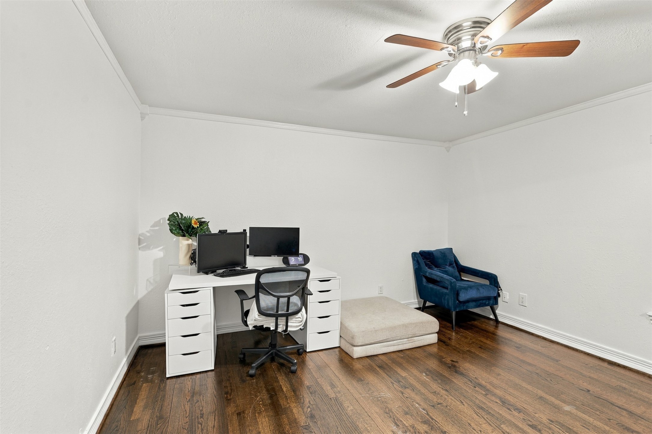 Bright and spacious home office with elegant hardwood floors, featuring a modern desk setup and a comfortable seating area under a ceiling fan.