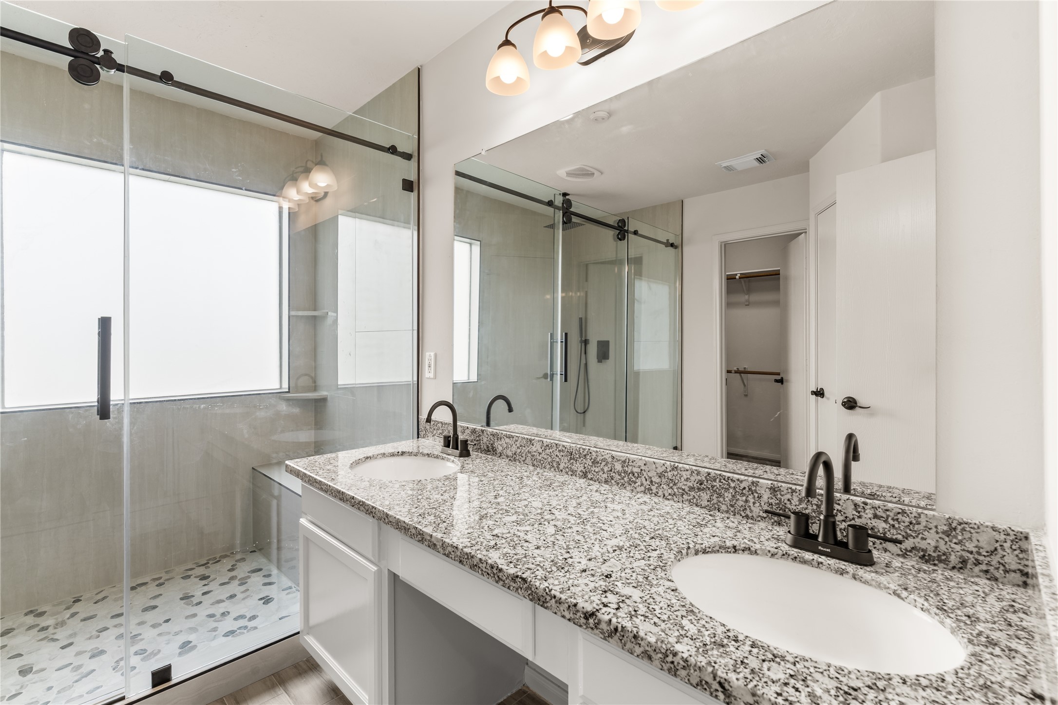 Beautifully updated primary bathroom featuring granite countertops, dual sinks, and modern finishes.