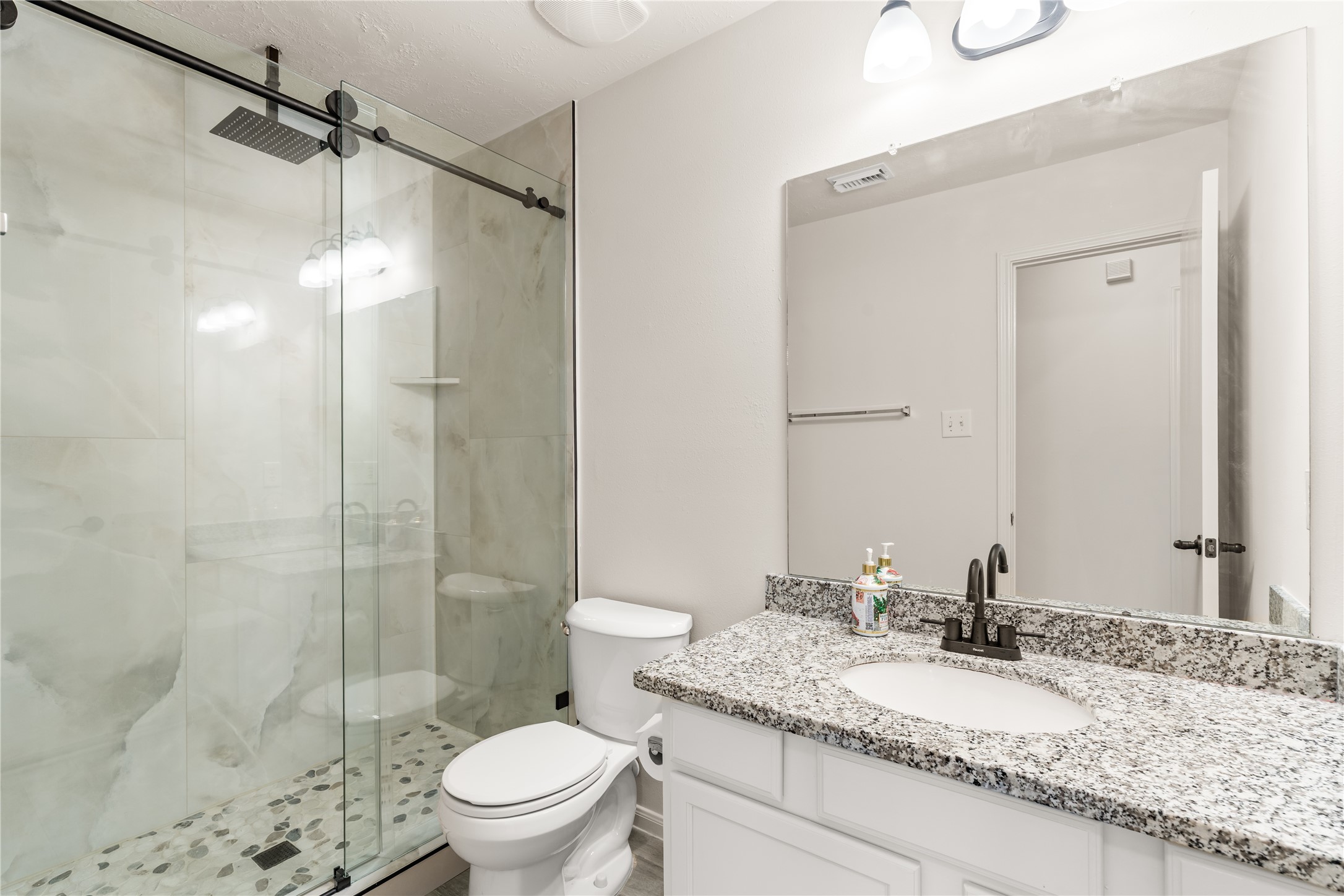 Updated secondary bathroom featuring granite countertops, modern fixtures, and a frameless glass shower.