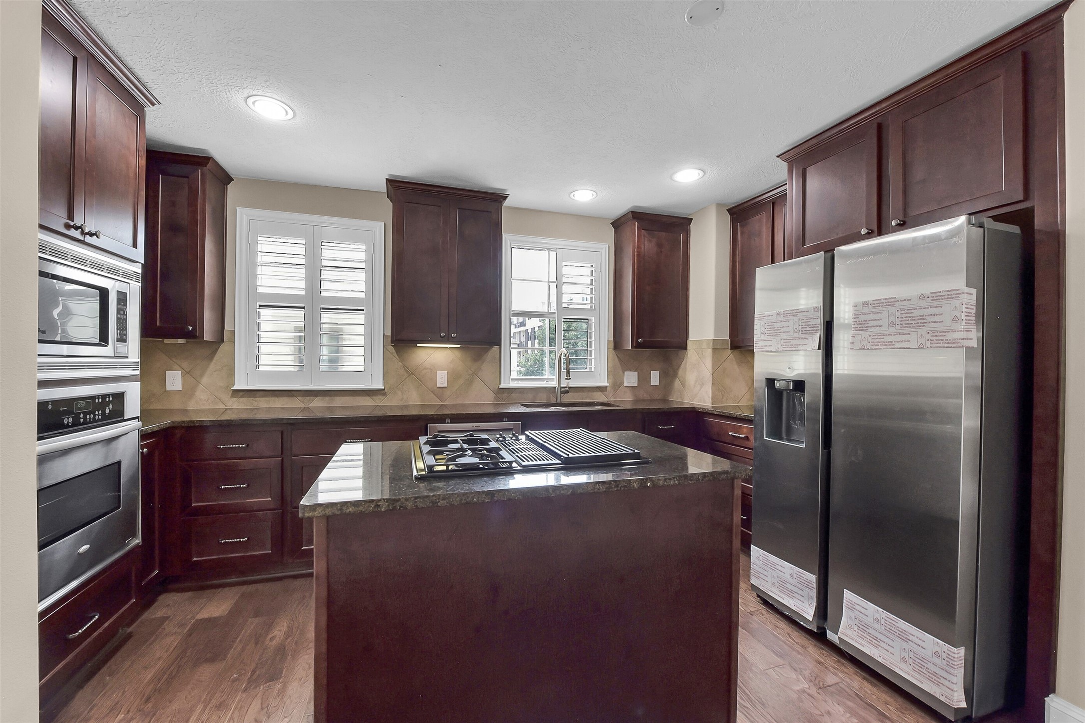 The island kitchen features a gas cooktop, stainless steel appliances, under cabinet lighting, granite counter tops, tile backsplash and upper and lower cabinets.