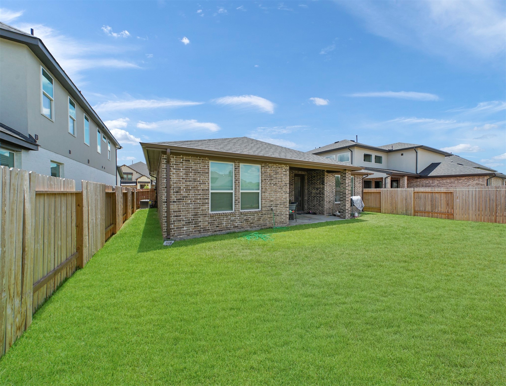 The brick exterior carries around to the rear of the home, where a fenced side yard and generous green space surround the outdoor living area.