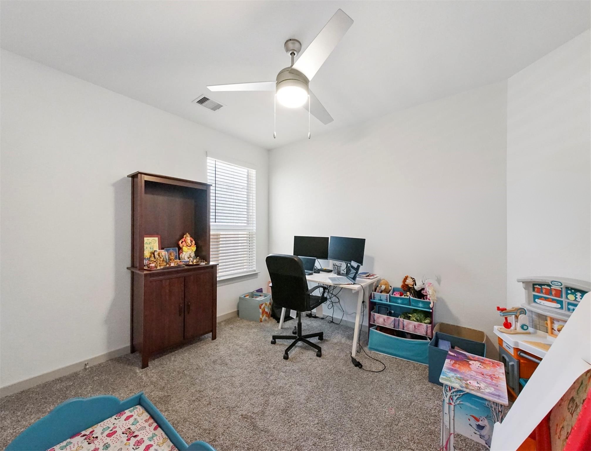 This flexible secondary bedroom adapts easily as a guest room or a dedicated home office, complete with a ceiling fan and a window with blinds.