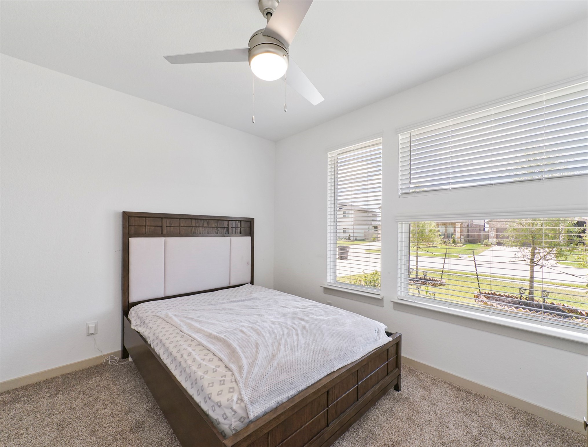 Sunlight pours through oversized windows in this front-facing secondary bedroom, creating an airy, open feel with views of the landscaped front yard.