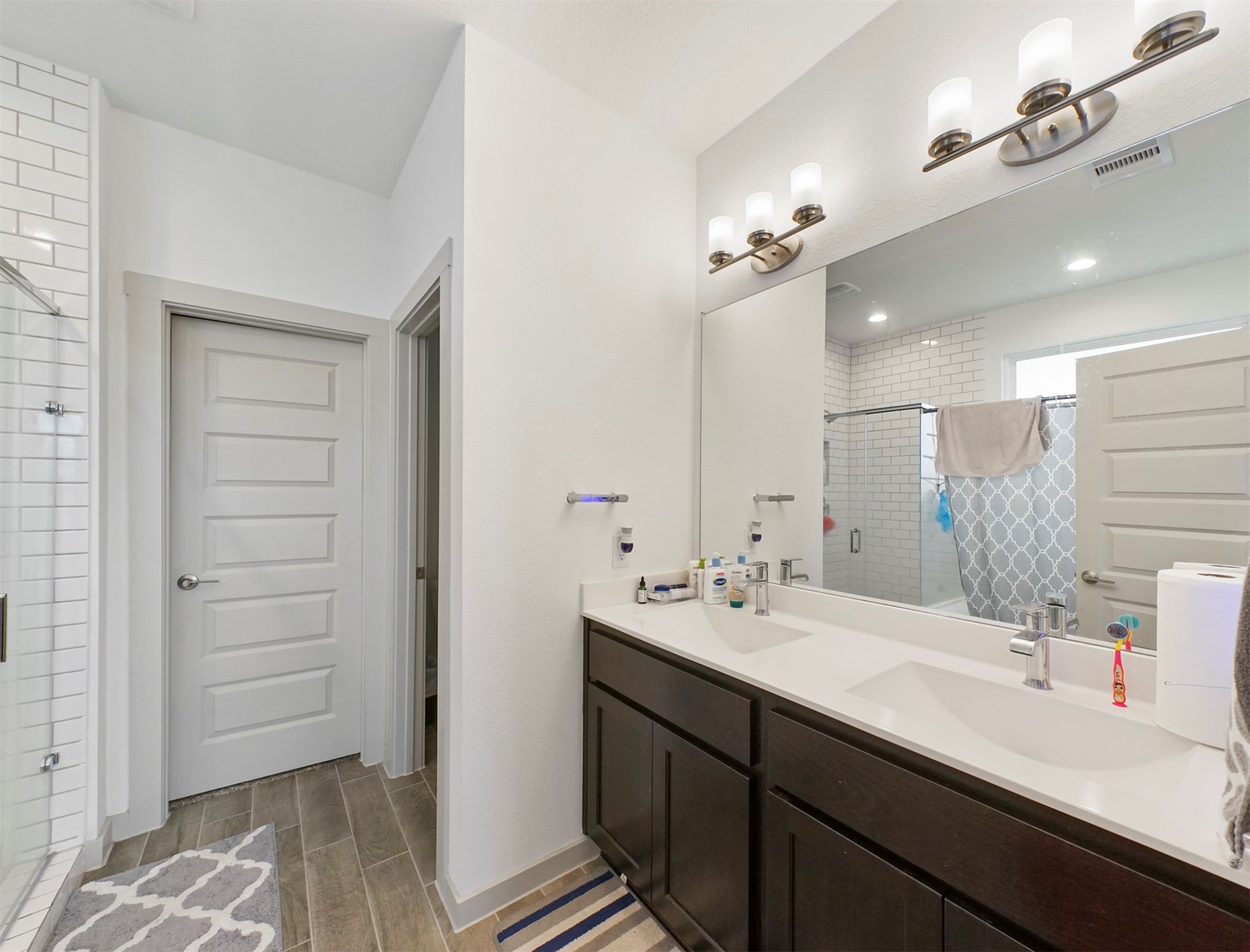 The ensuite bath offers a double-sink vanity with espresso shaker cabinetry, white countertops, a wide mirror, and brushed nickel light fixtures.