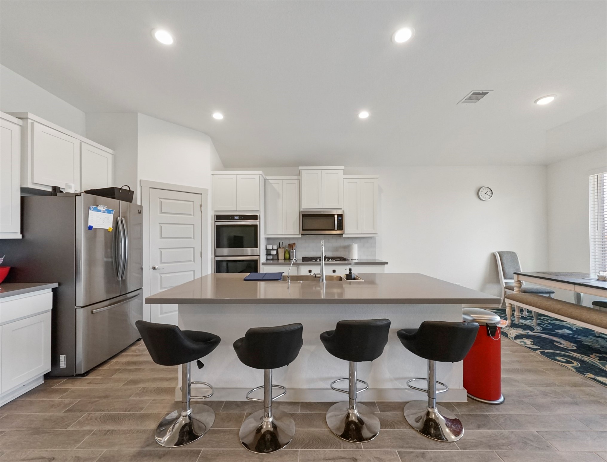 The kitchen is anchored by a large island with durable countertops and seating space. Its surrounded by white shaker cabinetry and stainless steel double wall ovens.