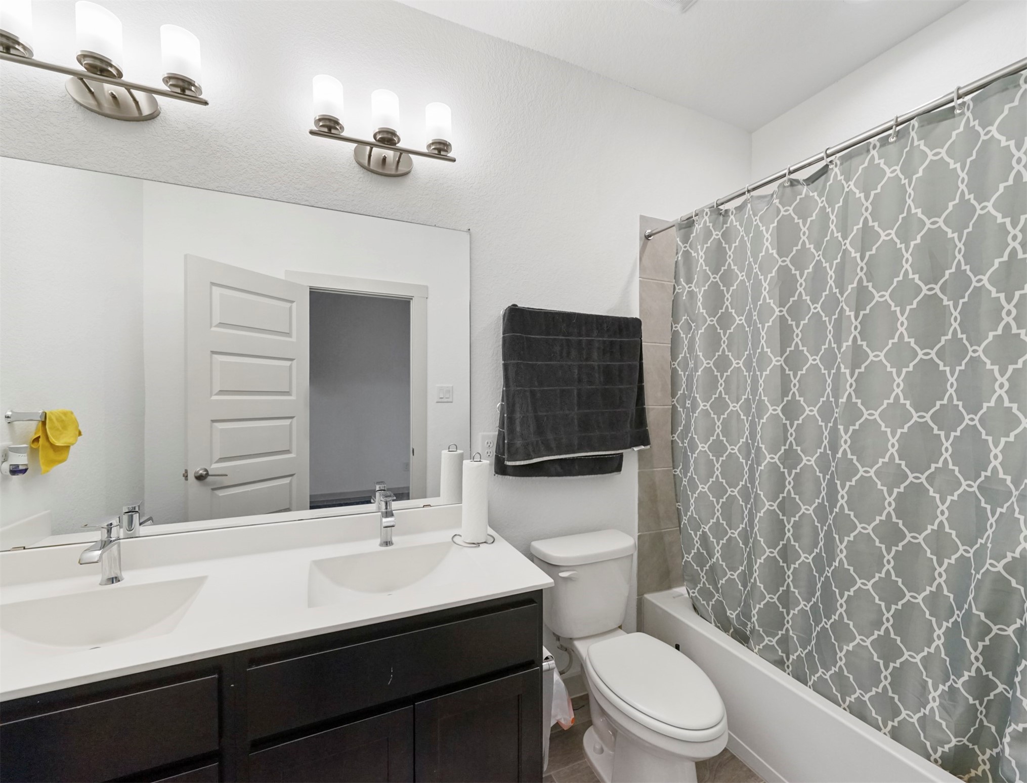 The secondary bathroom offers a double-sink vanity with espresso cabinetry, sleek chrome fixtures, and a tub/shower combination with a tile surround.