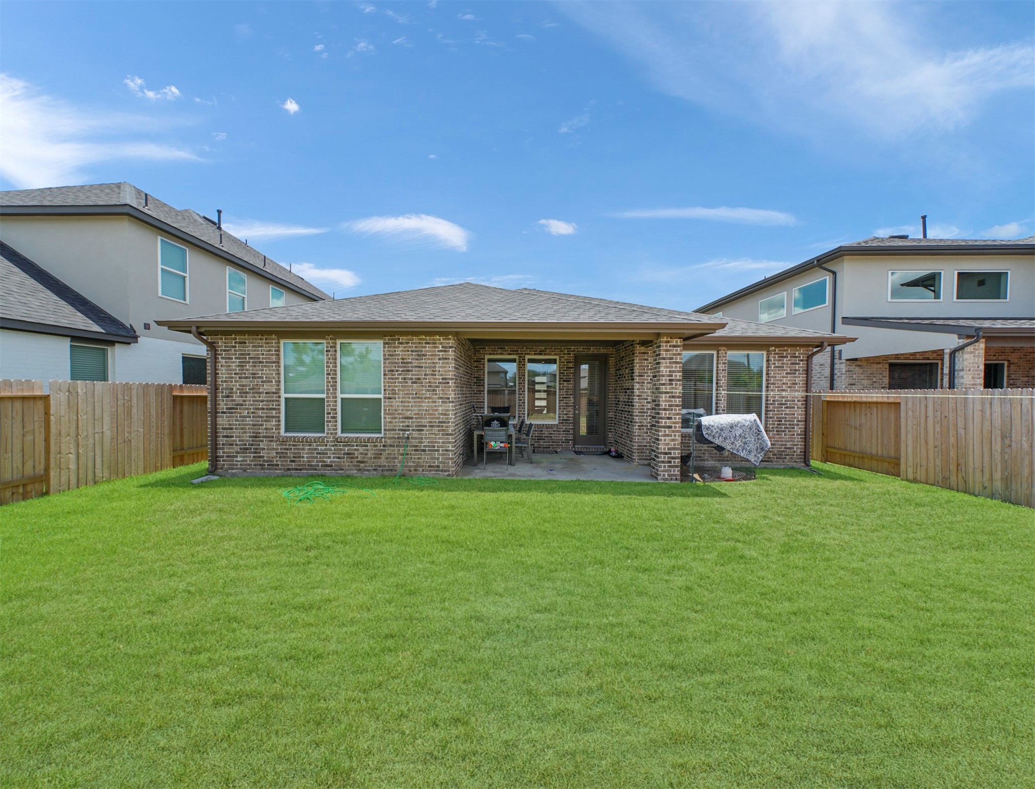 Step outside to a covered patio framed by brick columns, opening onto a fully fenced backyard with a wide, open lawn for outdoor dining and relaxing.