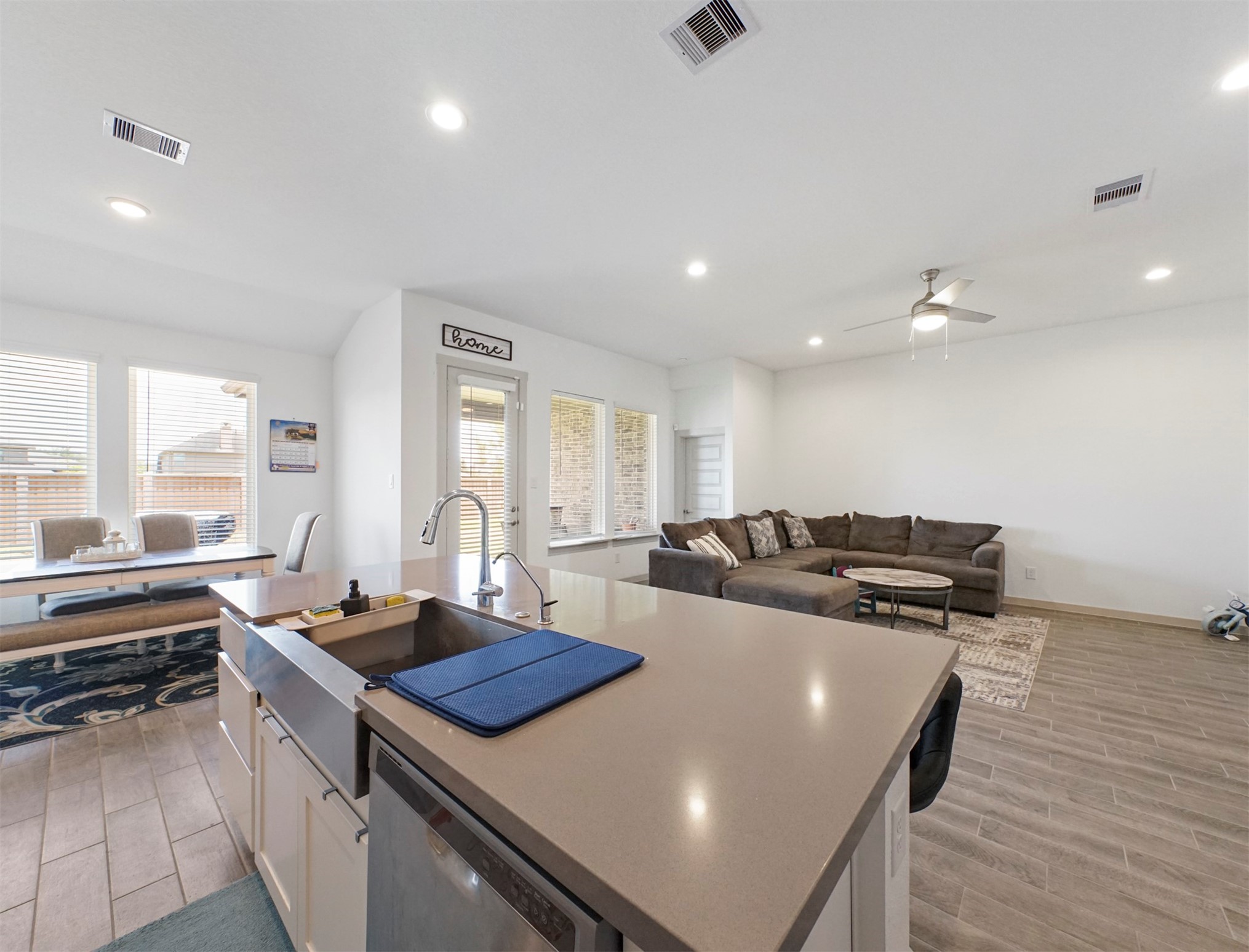 The island holds a stainless farmhouse sink and a dishwasher, and it overlooks the dining area and living room.